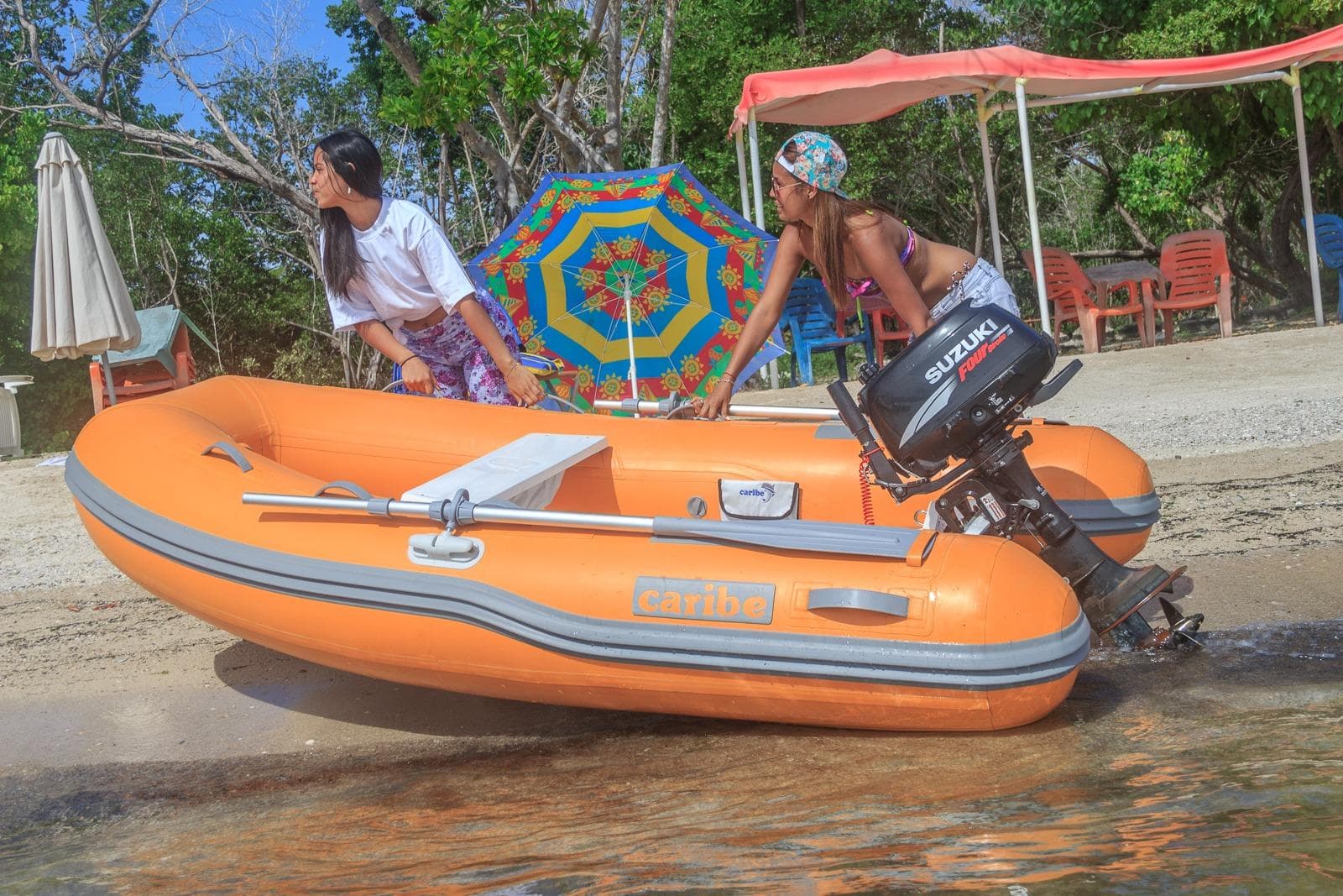 Two people with an orange Caribe L9 inflatable boat on a sunny beach.