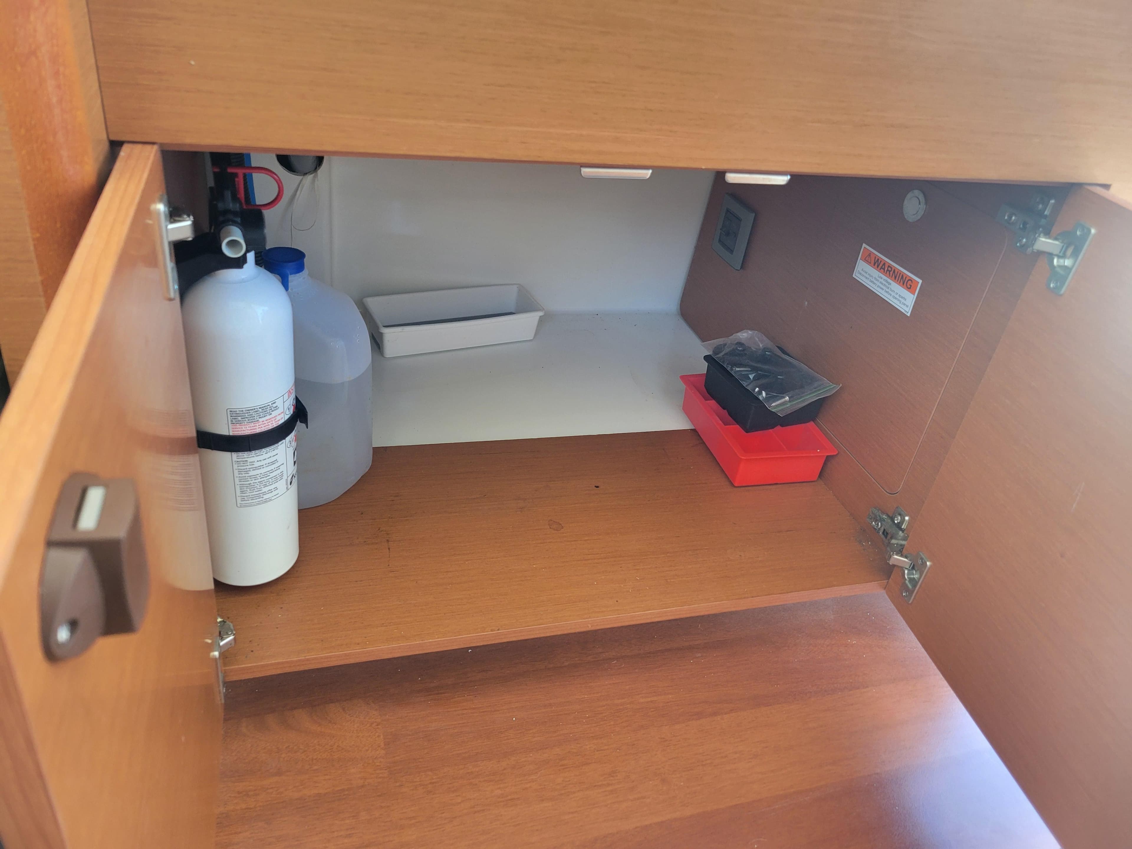 Open cabinet on Jeanneau Merry Fisher 855 boat, showing storage items and fire extinguisher.