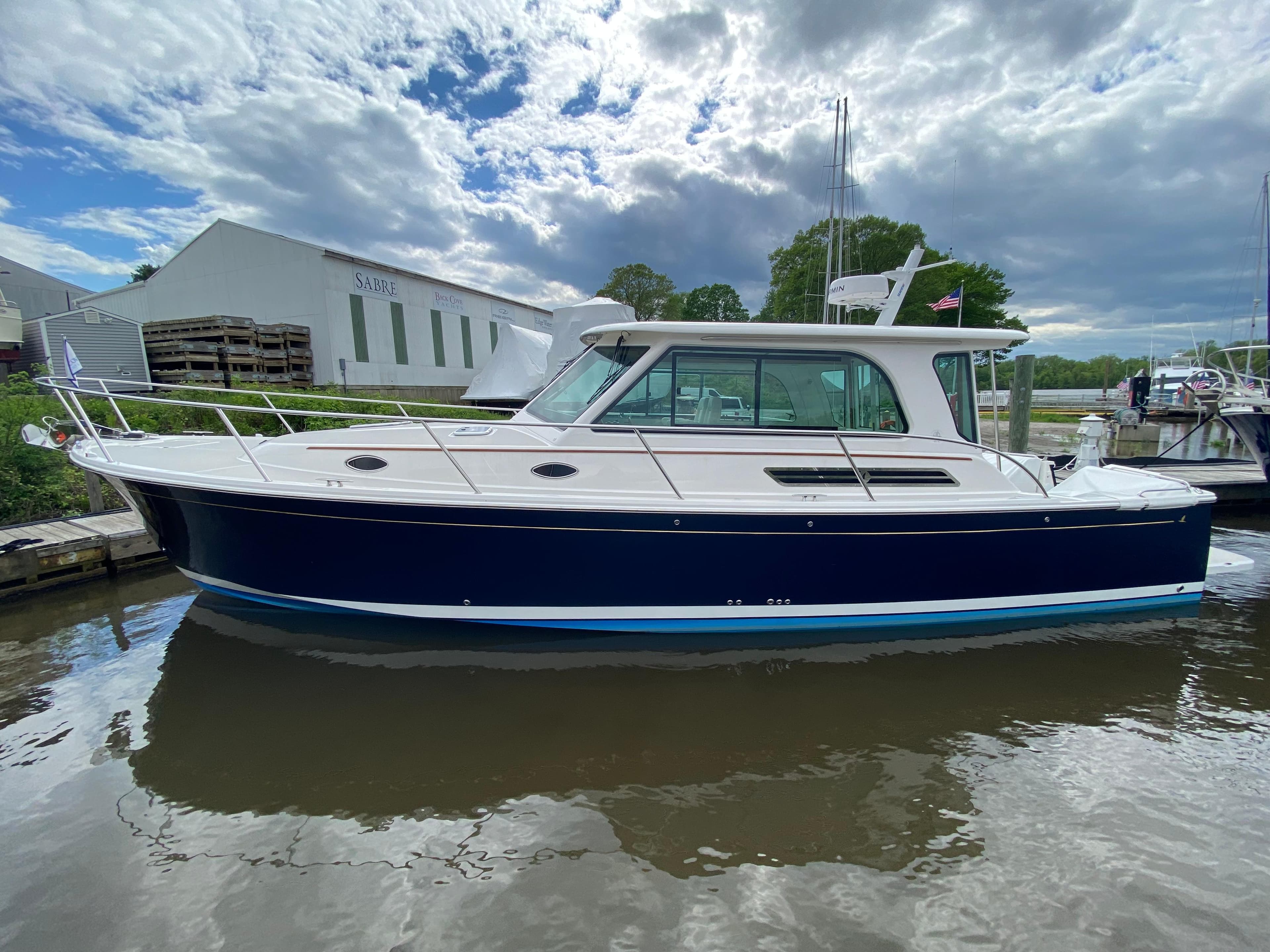 2025 Back Cove 37 Hardtop Express boat docked on a calm waterway under a cloudy sky.