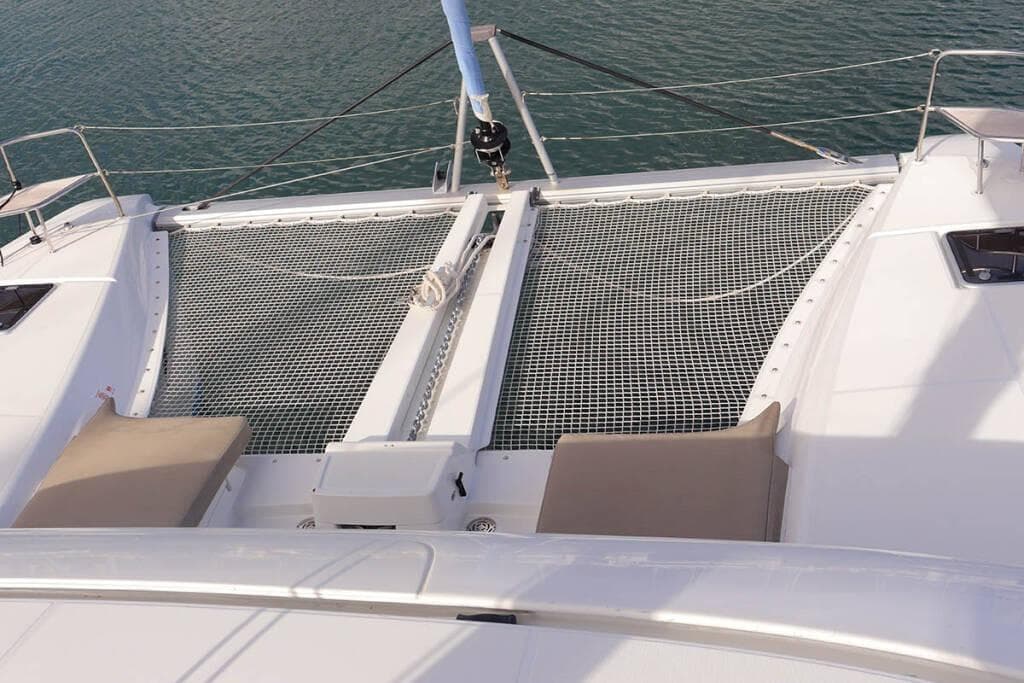 2023 Lagoon 46 catamaran deck with netting and sun loungers on calm water.