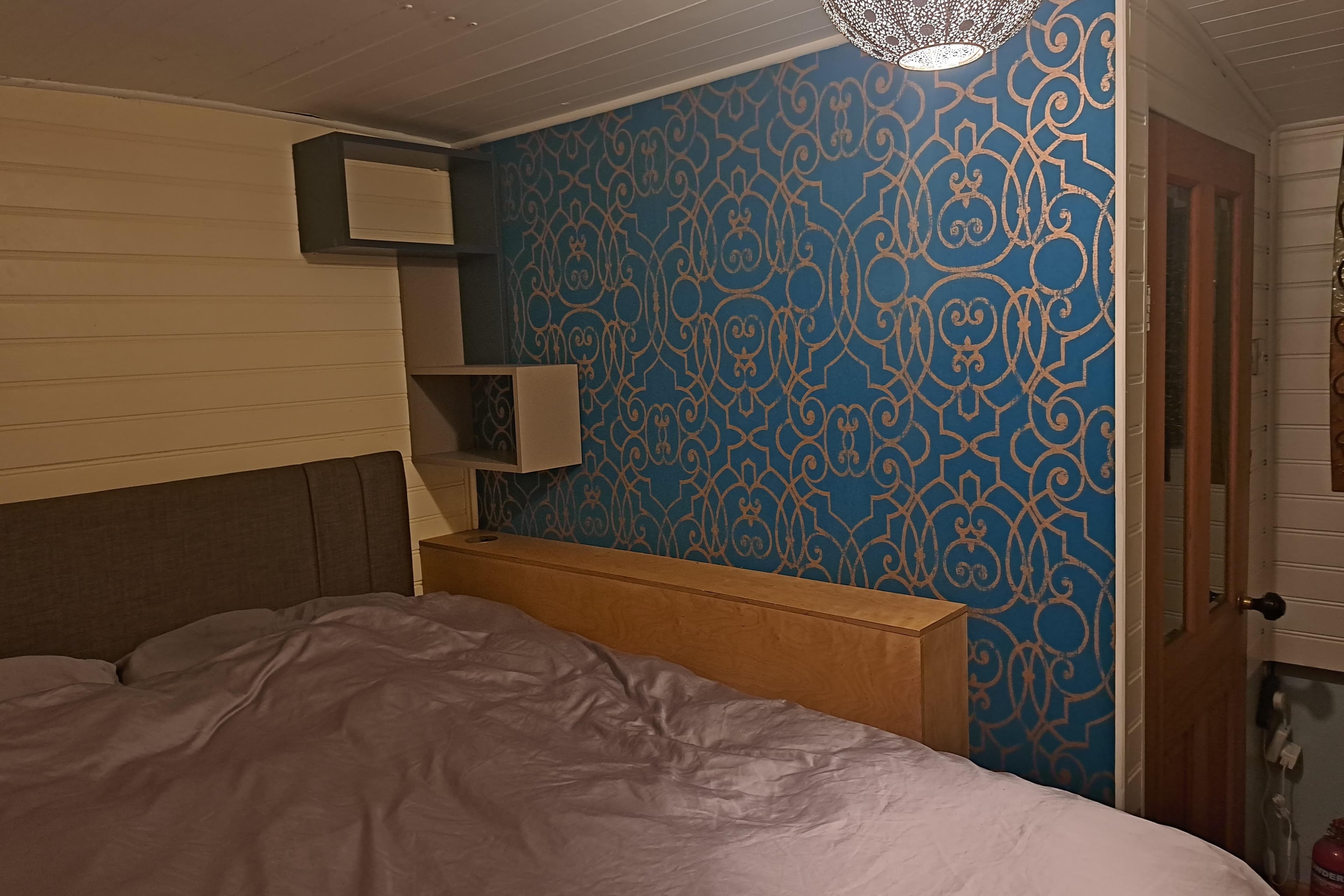 Cozy houseboat bedroom with patterned blue wallpaper and modern lighting, 2004 Barge model.