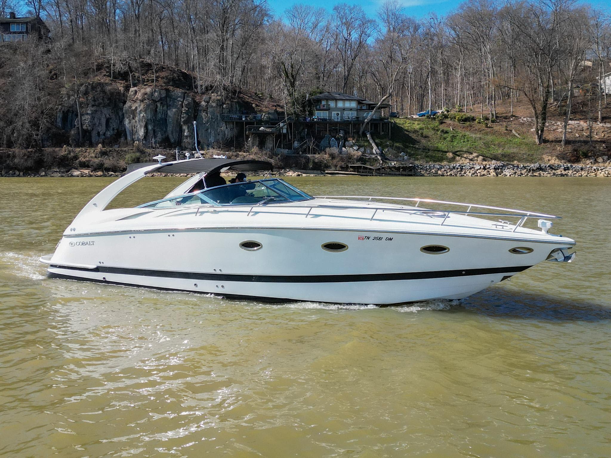 2004 Cobalt 360 boat cruising on a river with wooded shoreline.