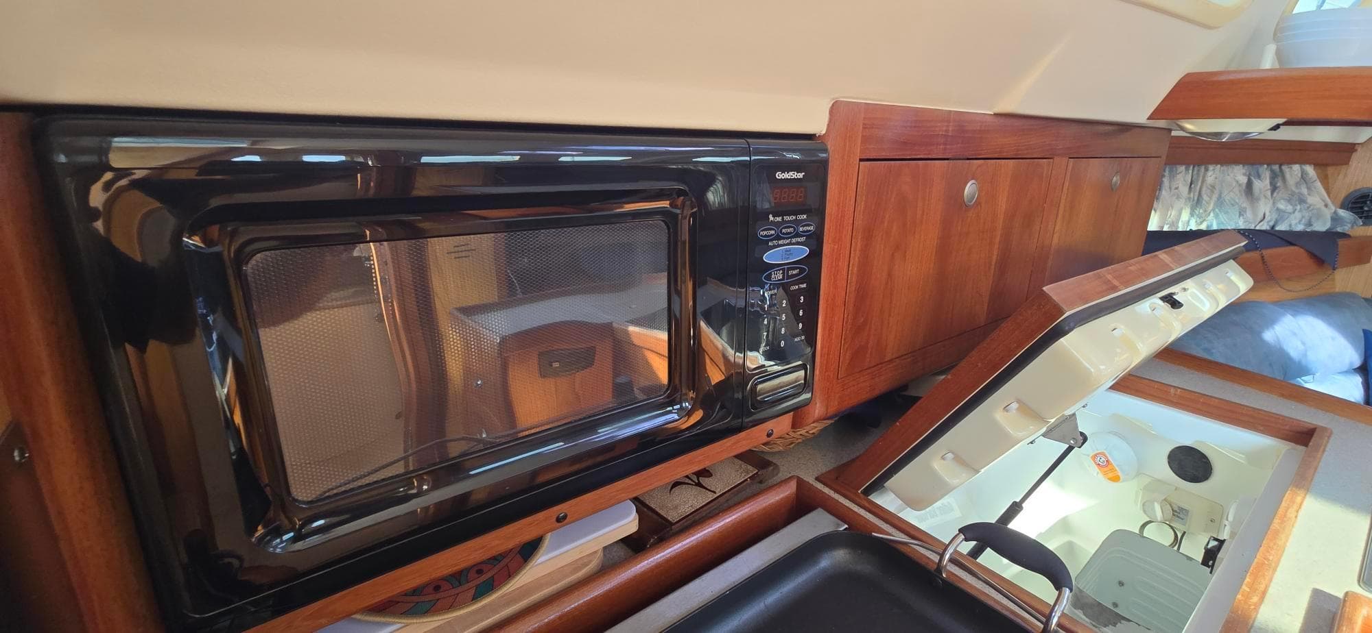 Microwave in 2000 Hunter 340 yacht kitchen with wooden cabinetry and open storage compartments.