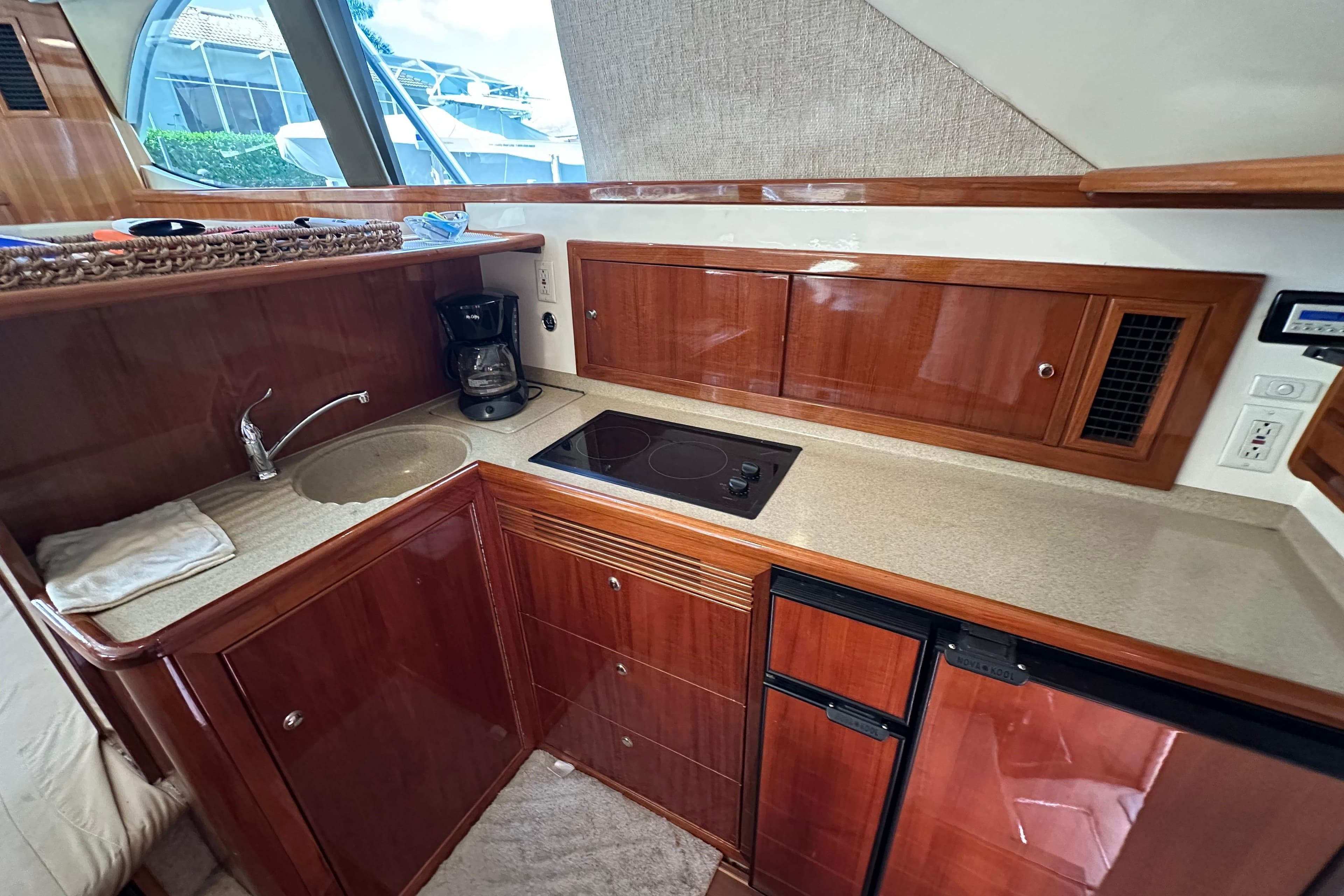 2002 Riviera 40 Flybridge yacht kitchen with wood cabinetry, sink, stove, and mini fridge.