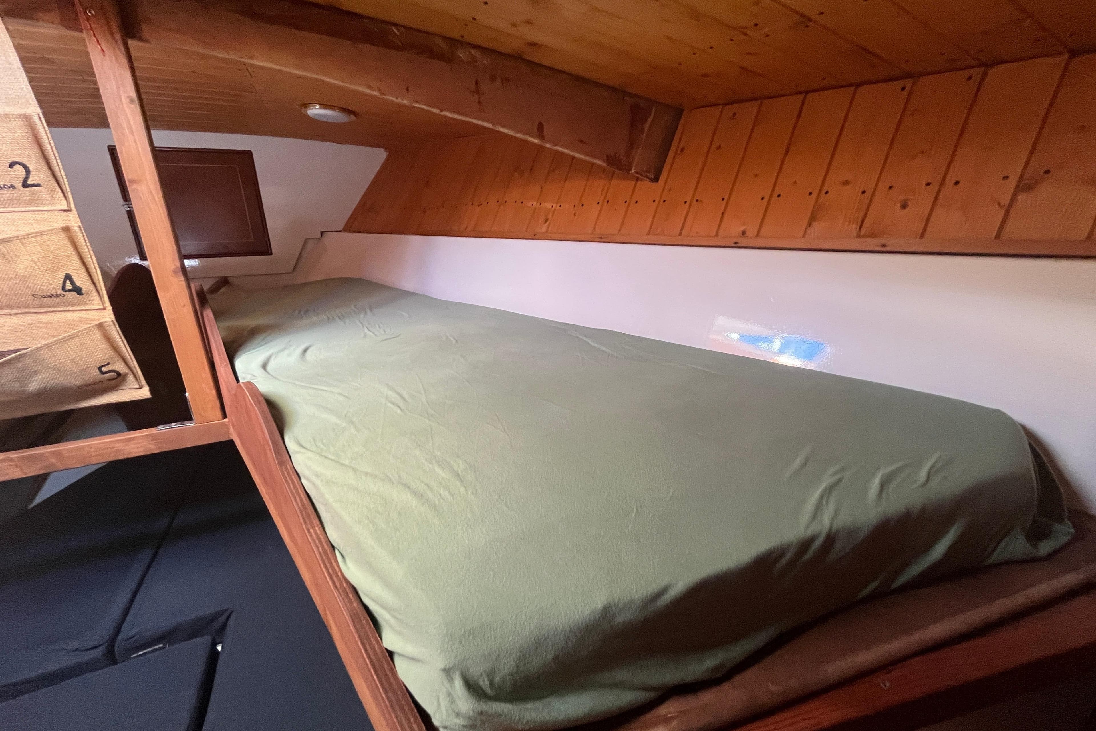 Cozy cabin interior of 1995 Belliure 41 yacht with wooden paneling and green bedding.