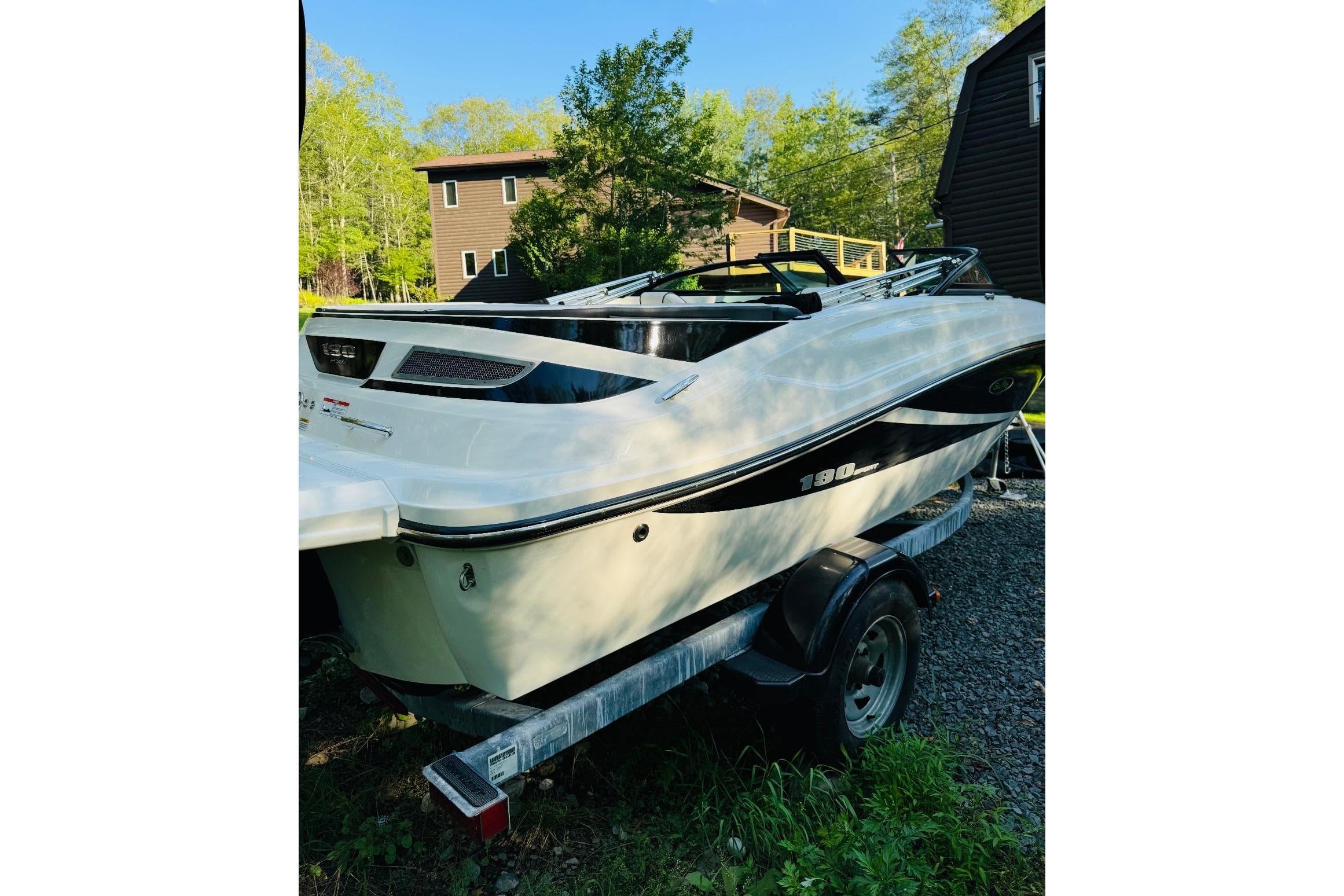 2013 Sea Ray 190 Sport boat on trailer, parked outdoors near trees and buildings.