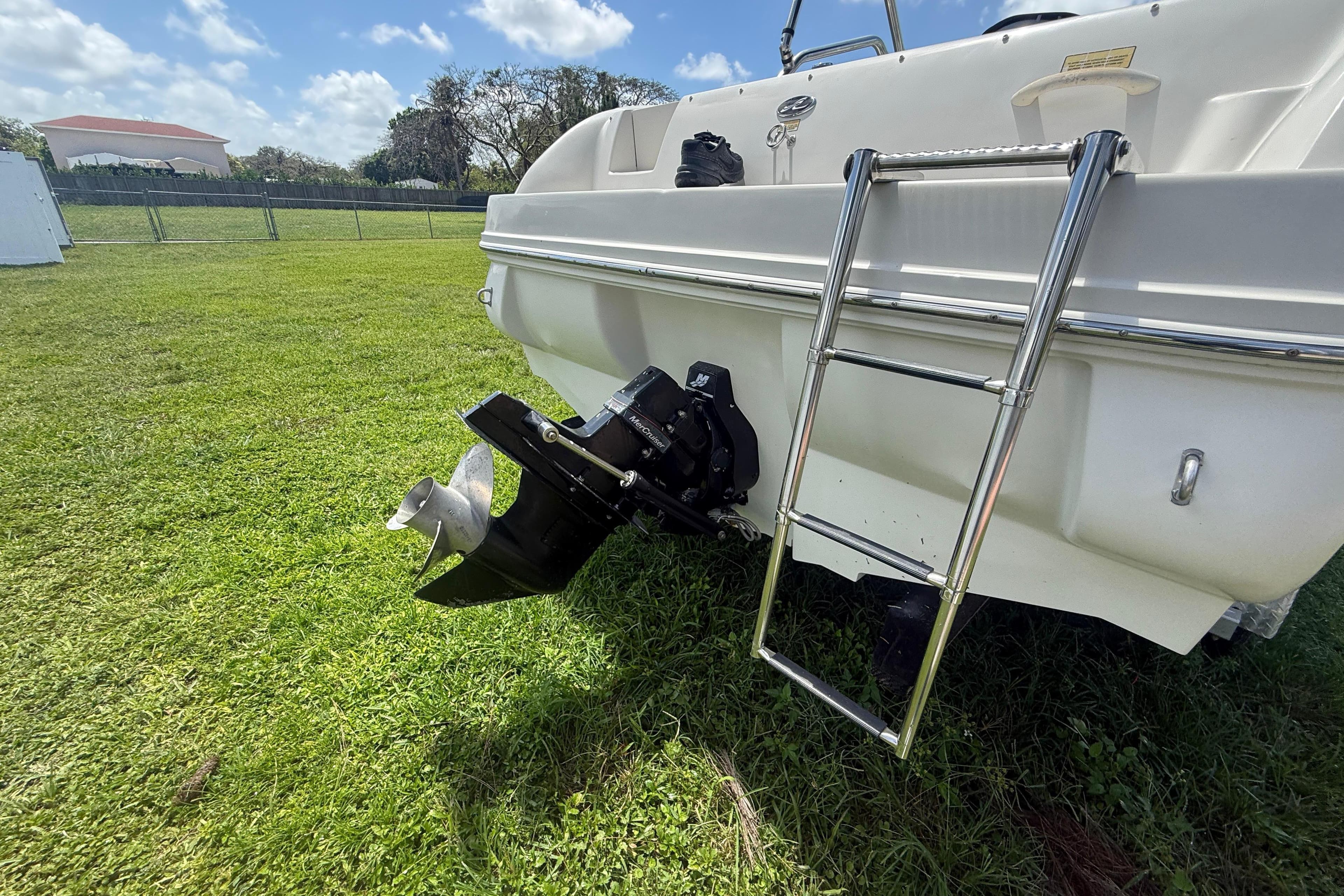 2004 Sea Ray 215 Weekender boat rear view with ladder and propeller on grass.