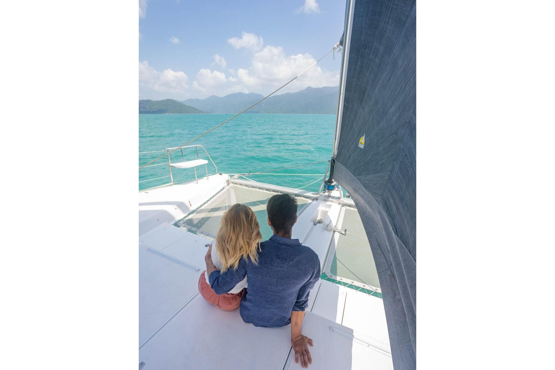 Couple enjoying ocean view on Seawind 1370 catamaran, 2026 model, under clear blue sky.