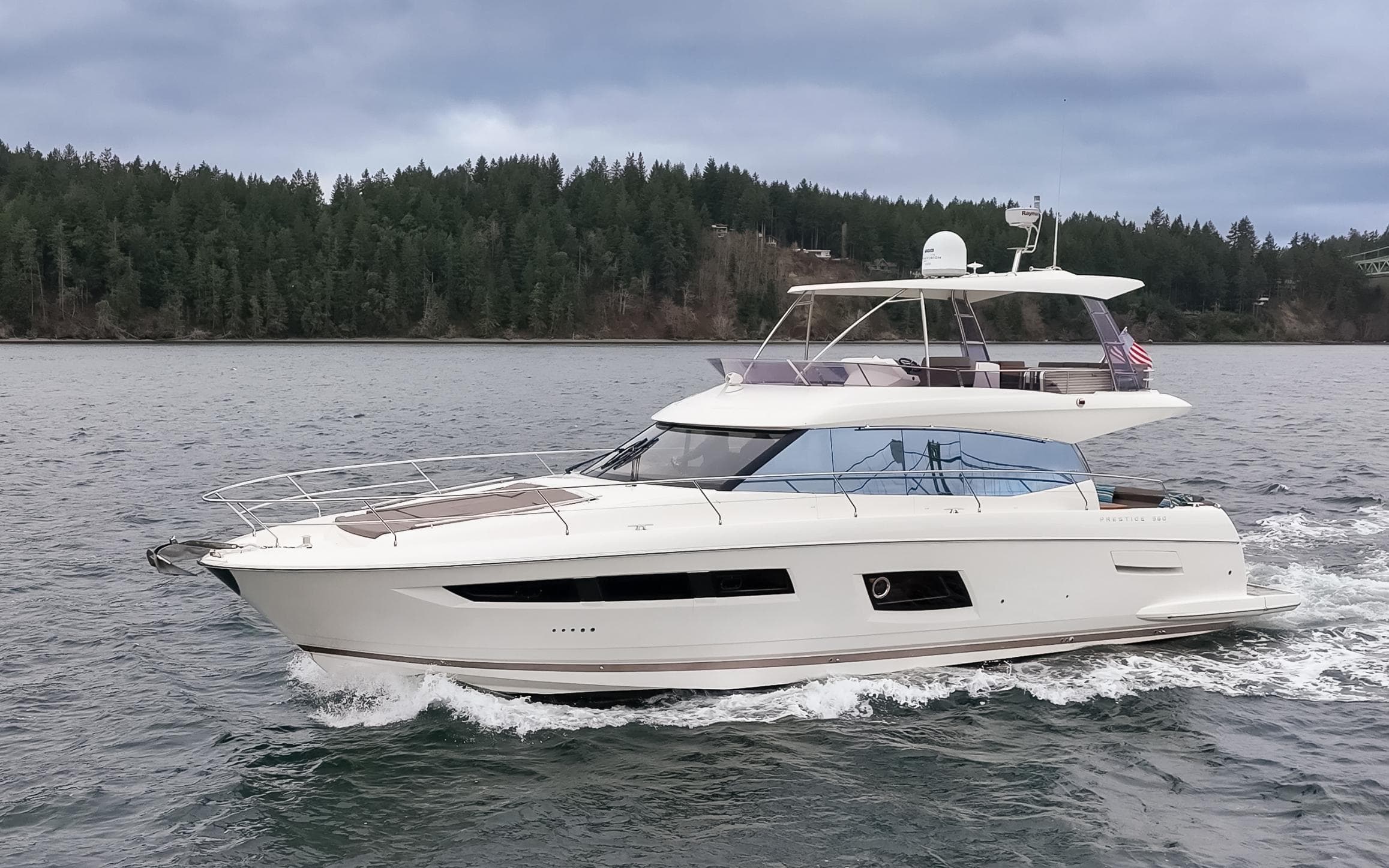 2017 Prestige 560 yacht cruising on a scenic lake with forested shoreline.