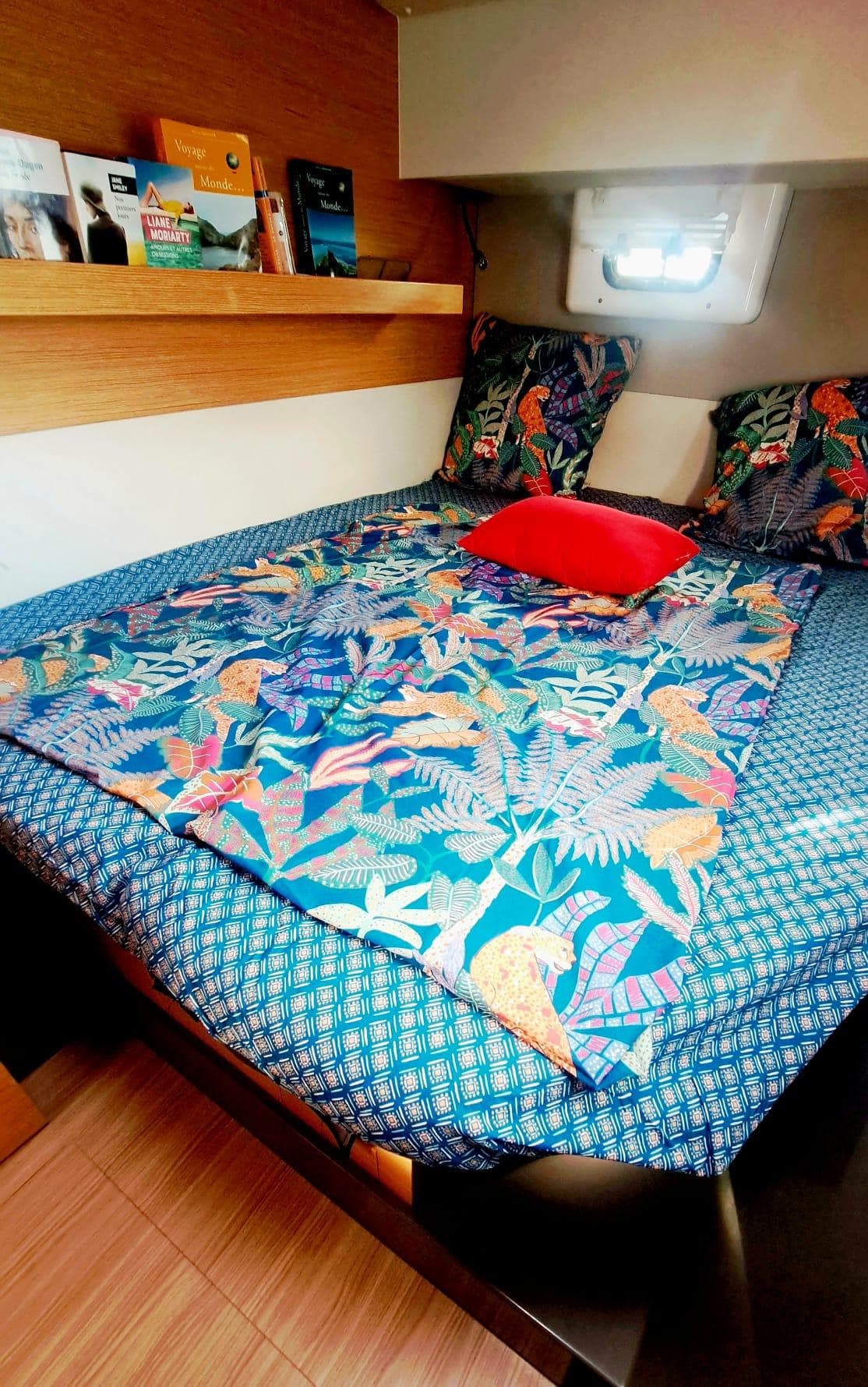 Cozy cabin interior of 2019 Nautitech 40 Open with vibrant bedding and books on shelf.