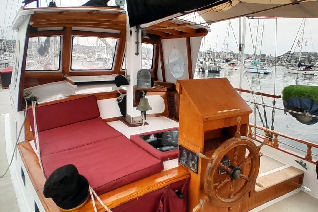 1974 Force Hudson 50 sailboat cockpit with wooden helm, red cushions, and marina view.