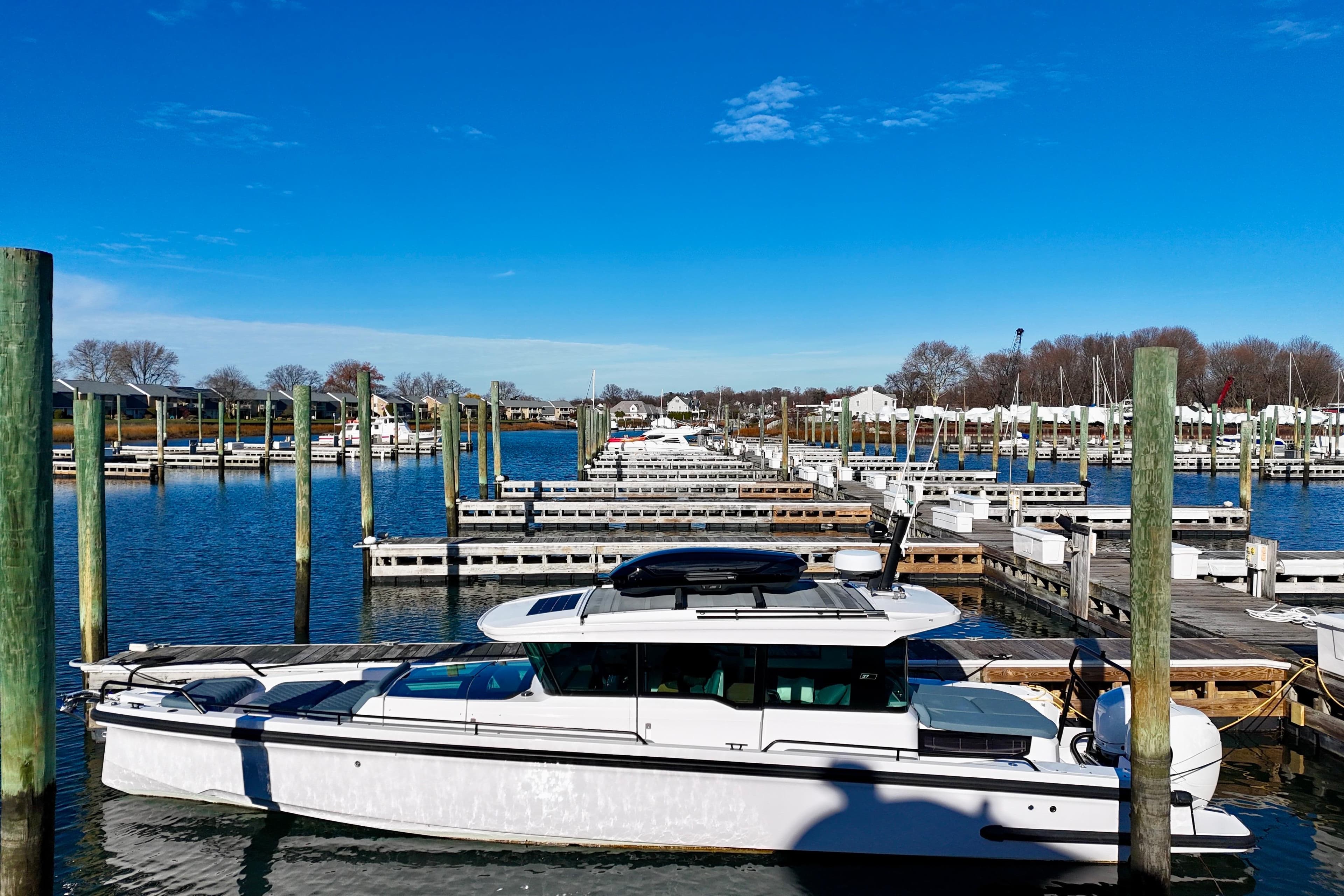 2023 Axopar 37 Cross Cabin docked in a serene marina under a clear blue sky.