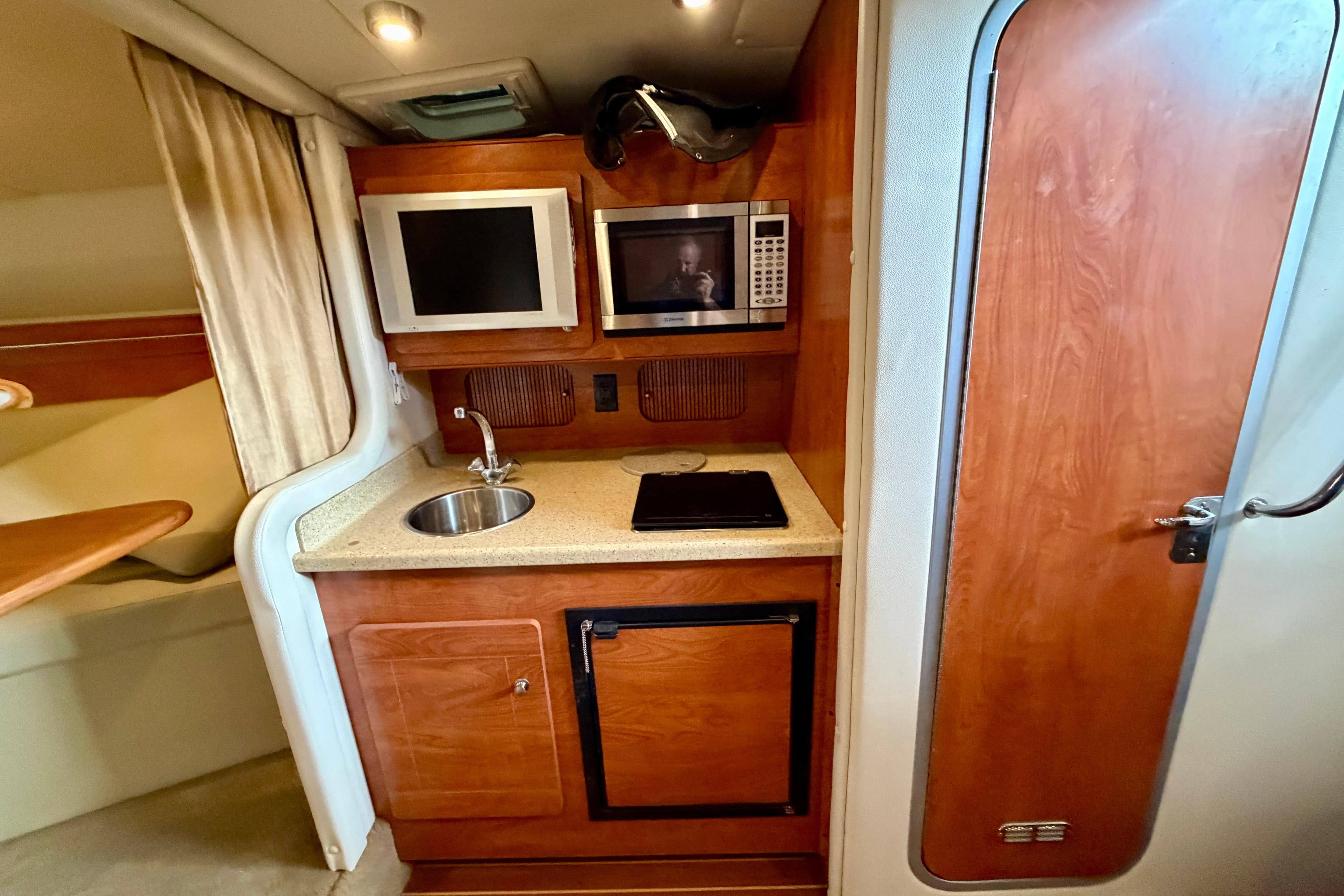 2006 Rinker 300 Express Cruiser interior kitchen with sink, microwave, and wooden cabinetry.