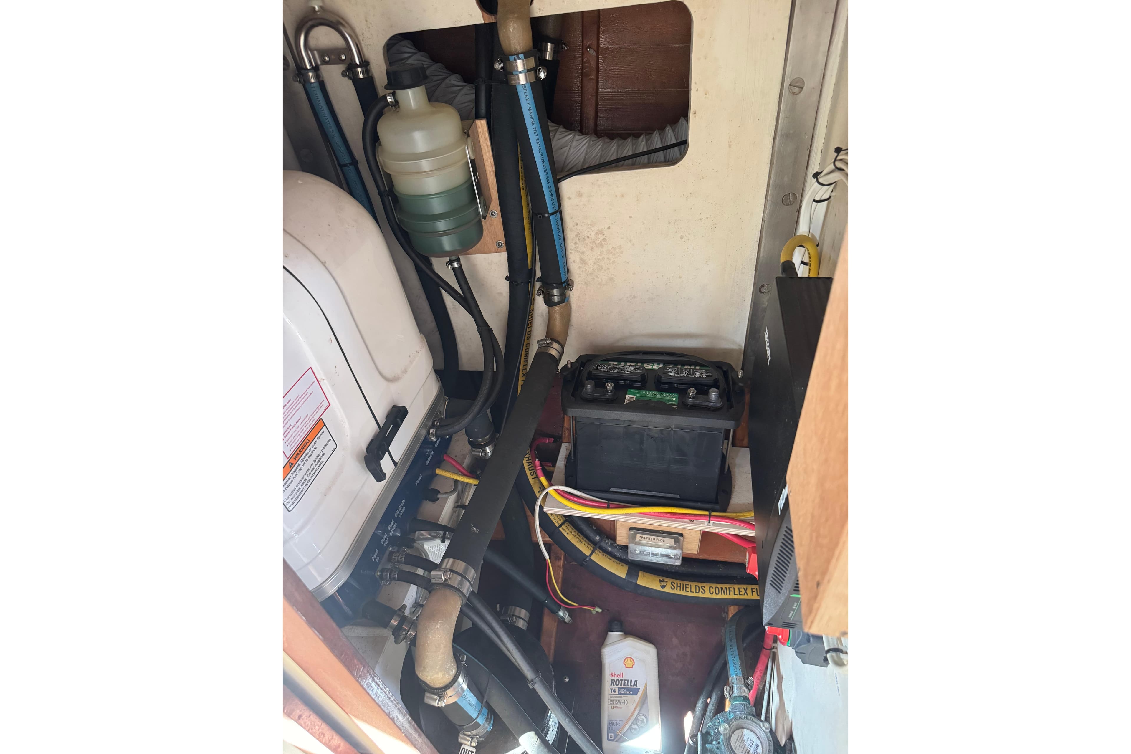 Engine compartment of a 1979 O.Lie-Neilsen 44 Cutter Rigged sailboat, showing battery and hoses.