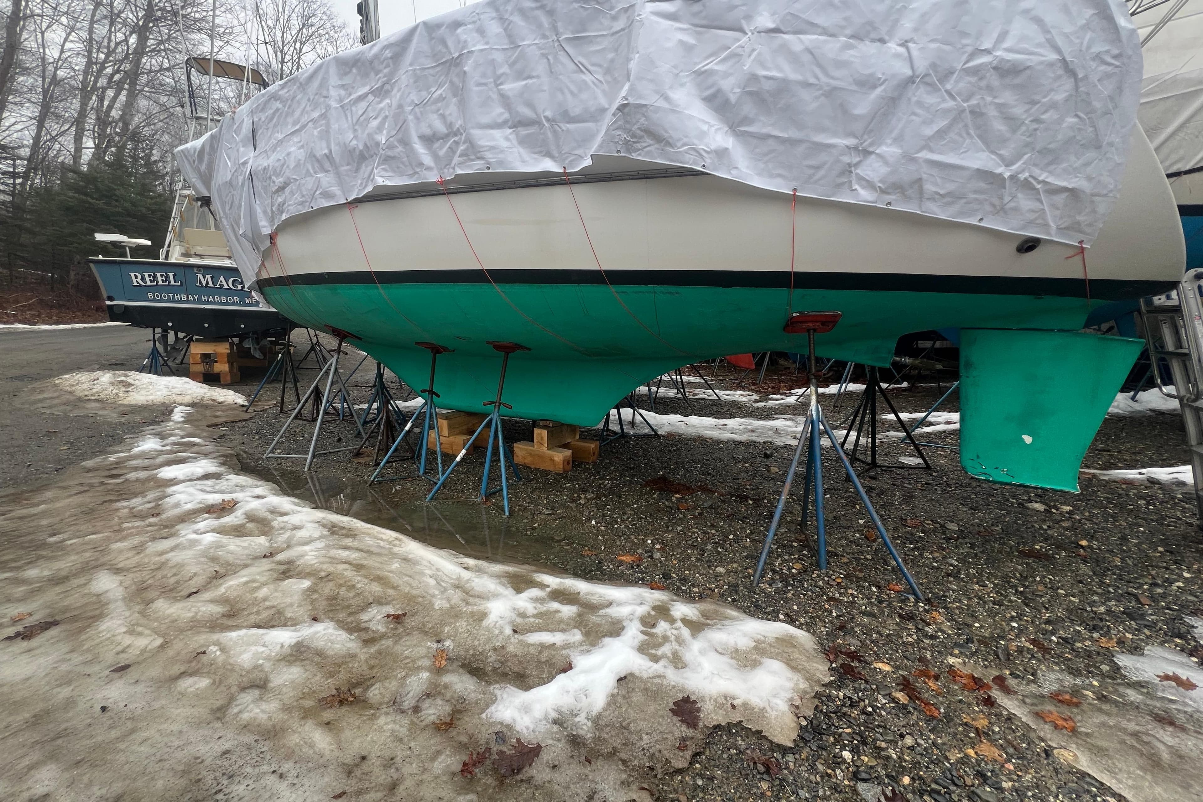 1993 Com-Pac Sloop sailboat on stands, covered, with snow and trees in the background.