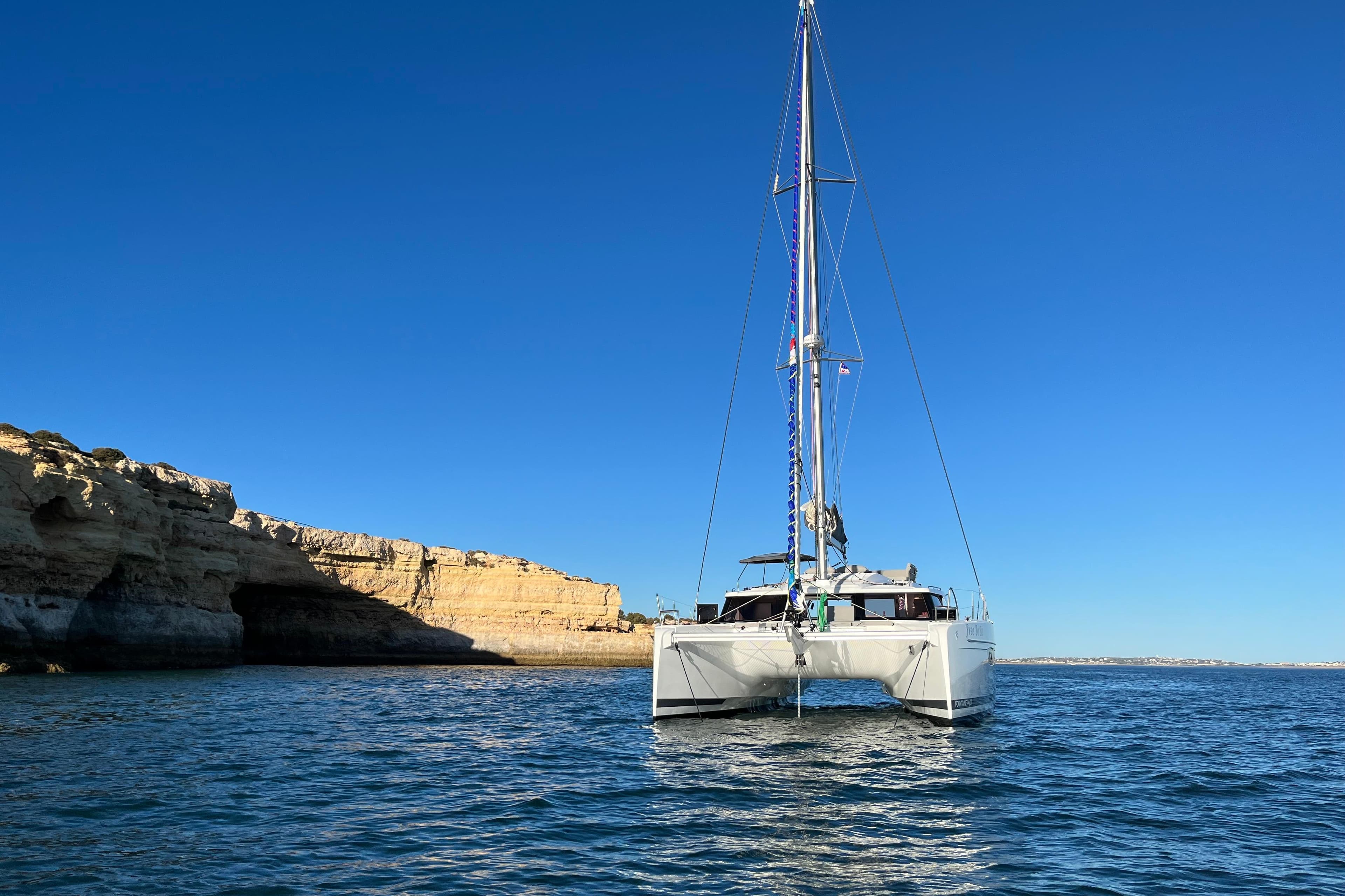 2022 Fountaine Pajot Elba 45 Catamaran sailing near rocky coastline under clear blue sky.
