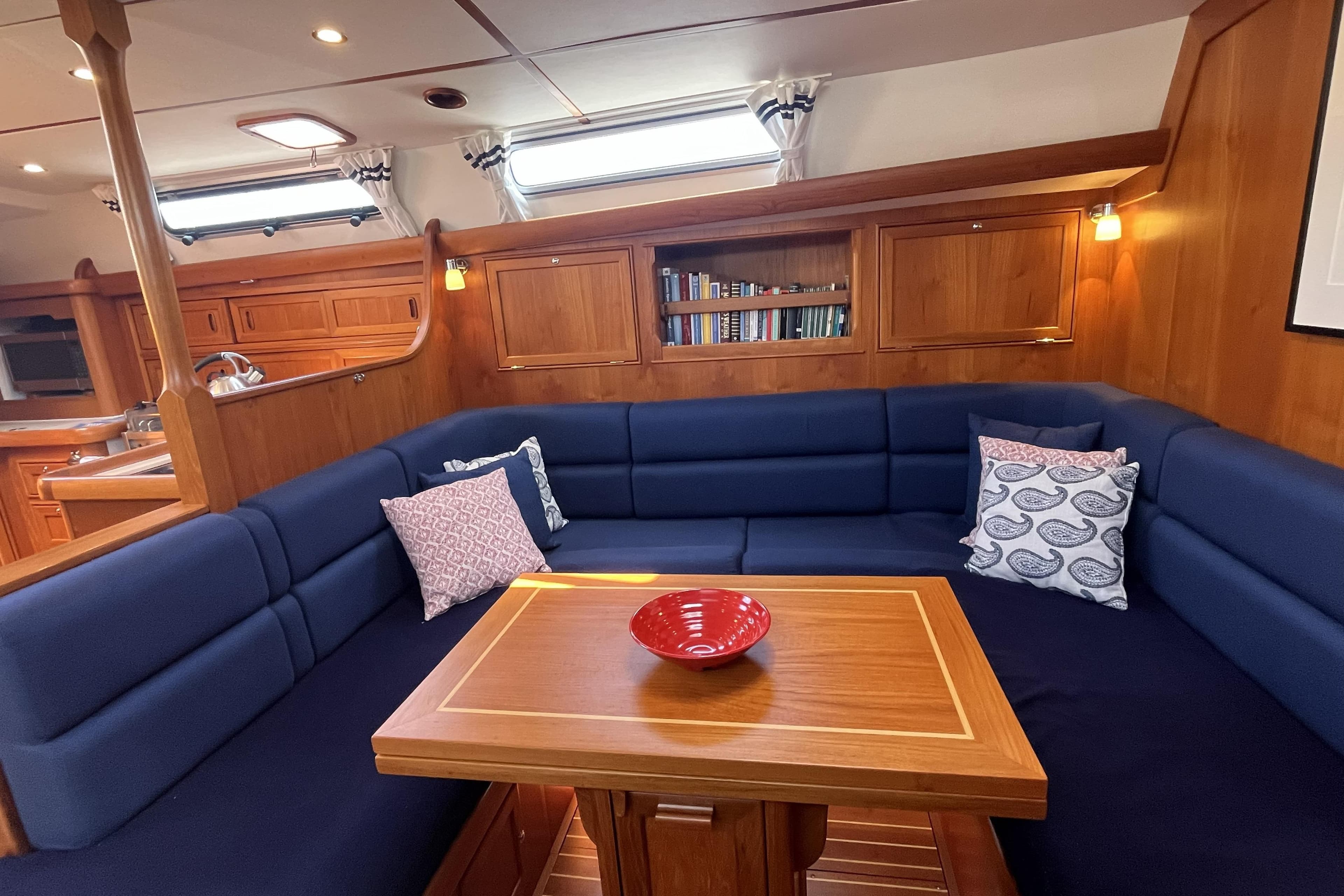 Luxurious 2017 Rustler 37 yacht interior with blue seating, wooden table, and bookshelves.
