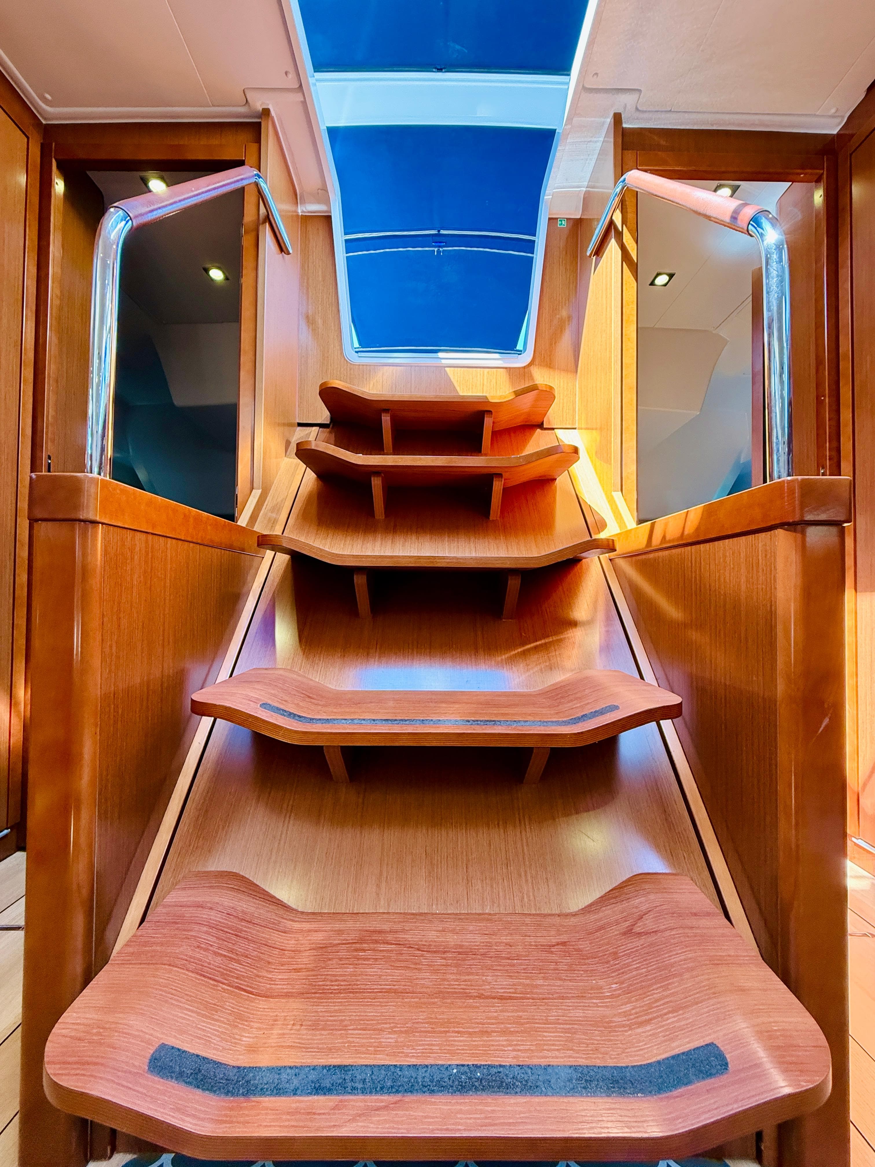 Interior staircase of 2015 Beneteau Oceanis 55 yacht with wooden steps and skylight.