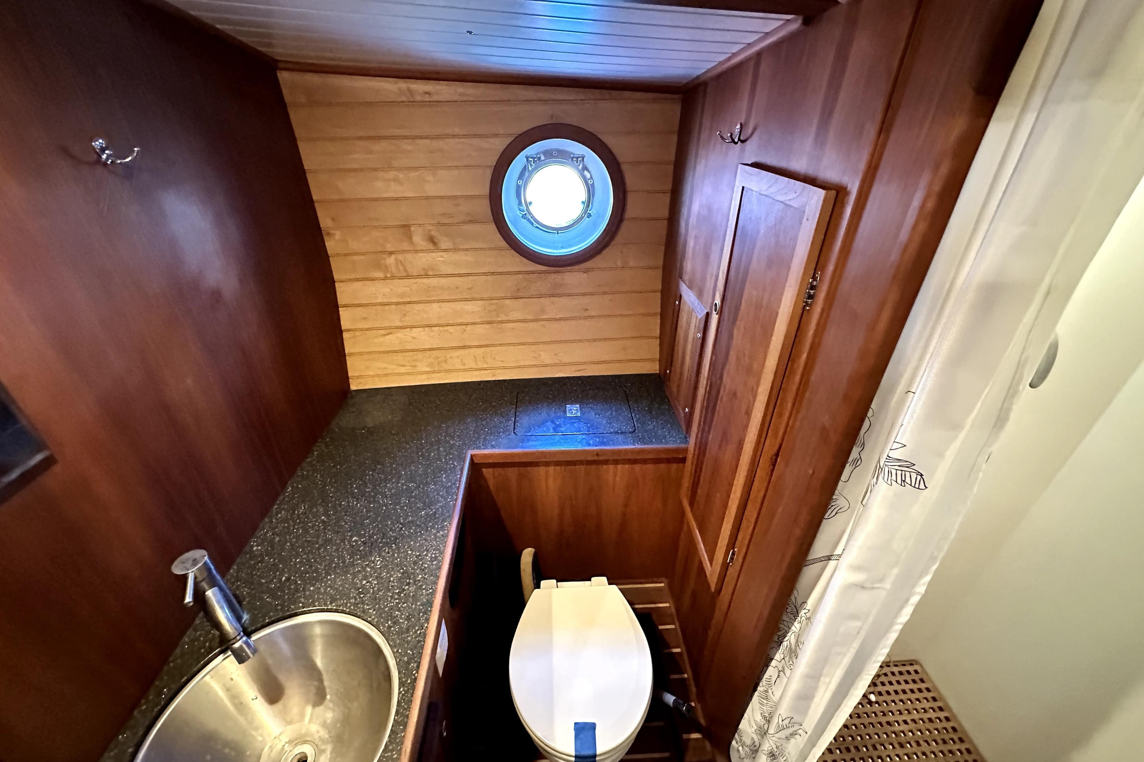 Wood-paneled boat bathroom with porthole, sink, and toilet on Custom Pacific Northwest 43, 2012.