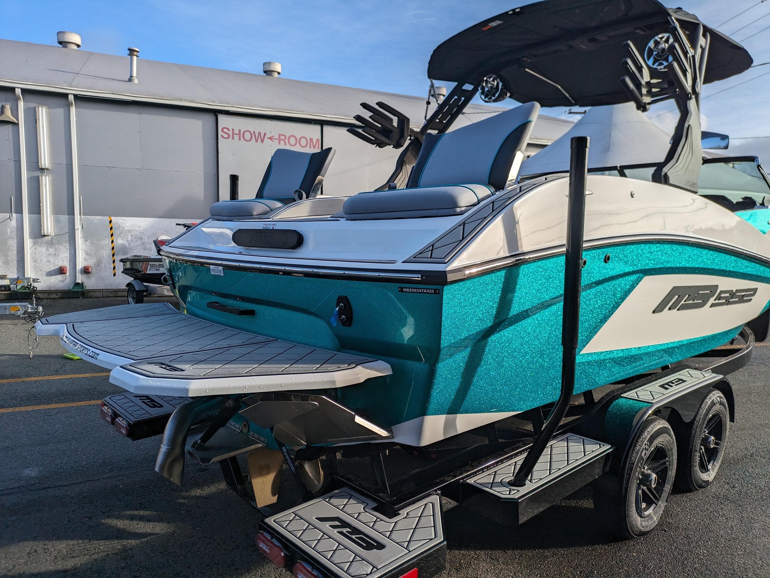 2025 MB B52-23 Alpha boat in showroom, vibrant teal color, on a trailer.