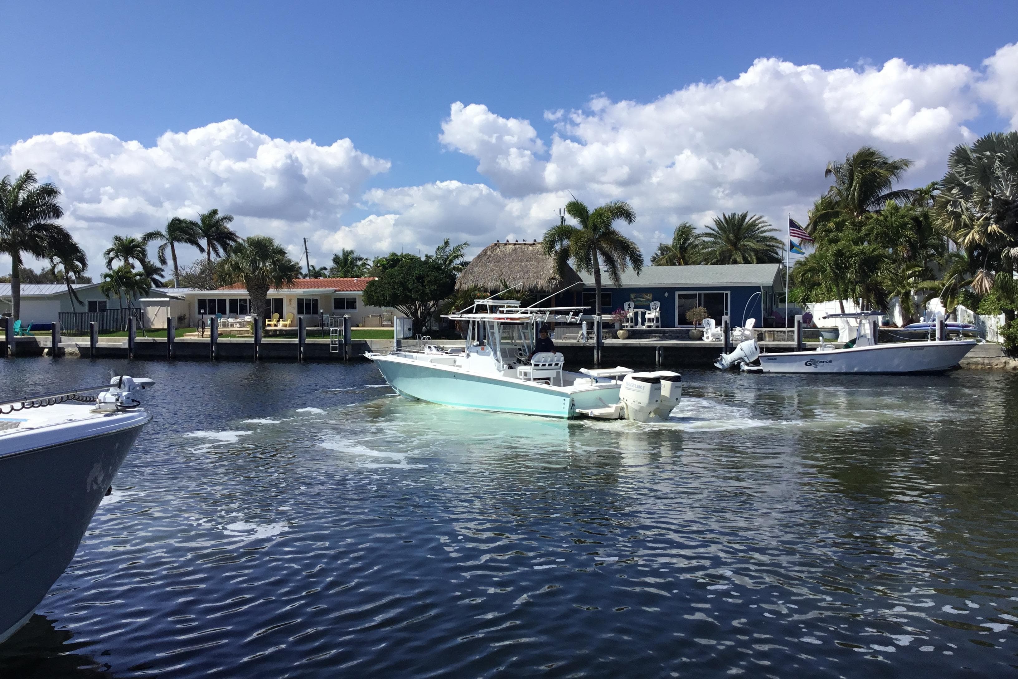 2000 Jupiter 31 Center Console boat cruising on a sunny waterfront with palm trees.