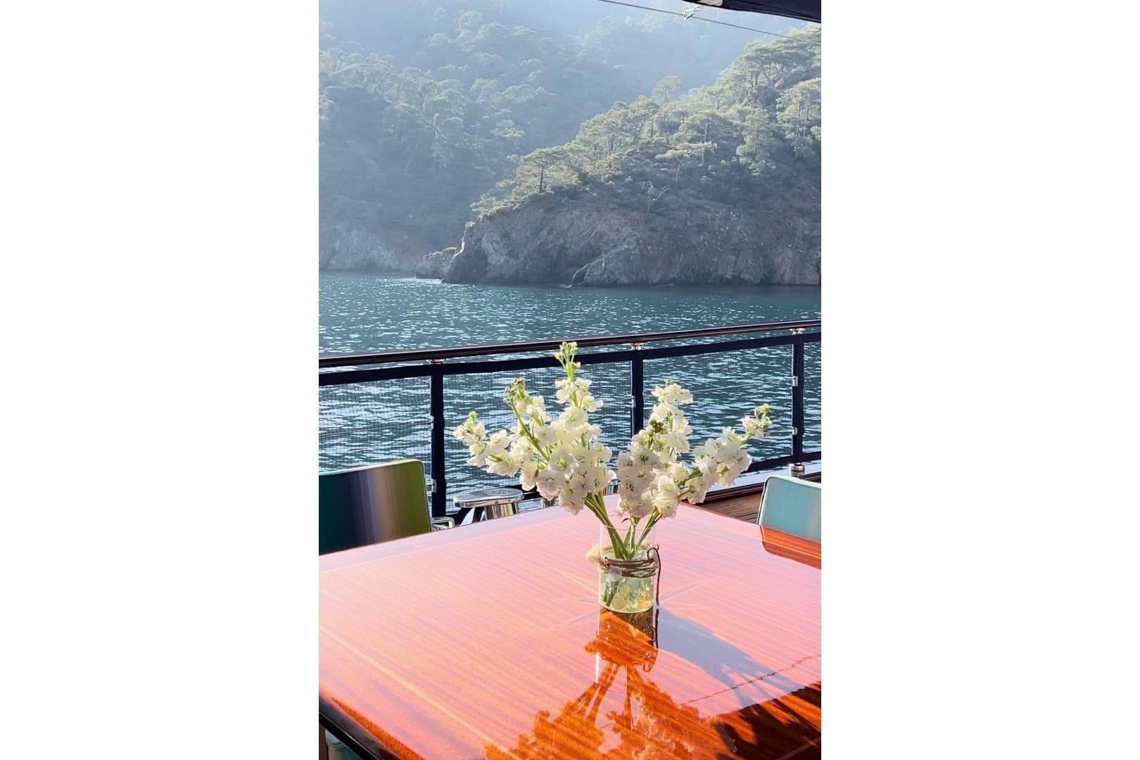 Elegant yacht table with flowers, overlooking serene waters and lush cliffs. Custom-Craft Steel Pax Navi 43 m, 2010.