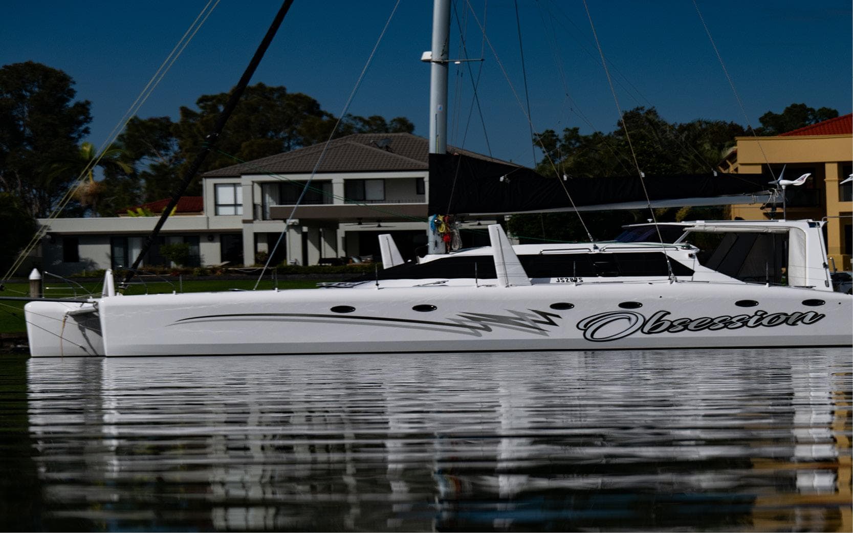 2017 Schionning Wilderness 1620 catamaran named "Obsession" docked near waterfront homes.