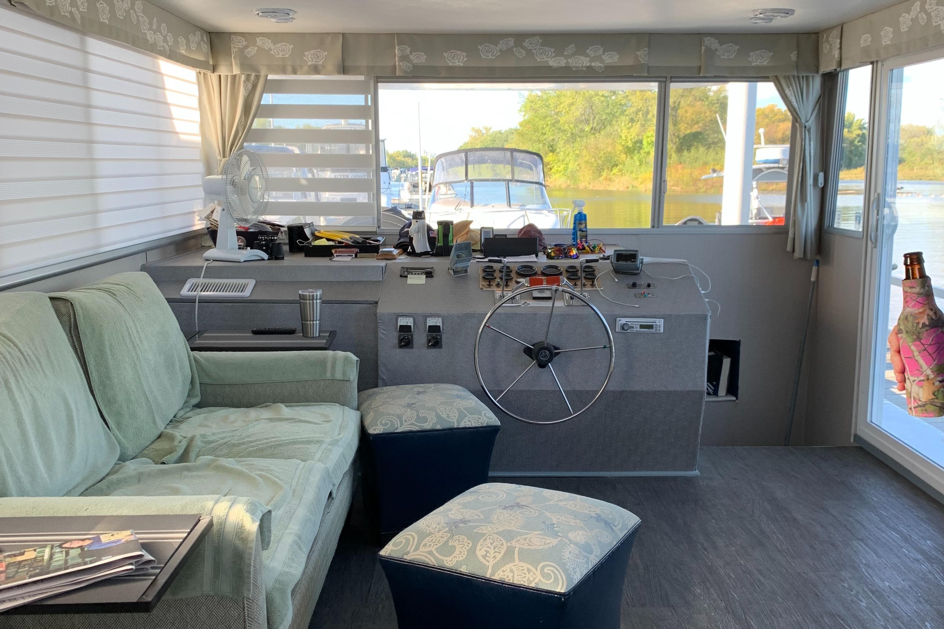 Interior of a 1977 Gibson Standard boat with helm, sofa, and scenic window view.