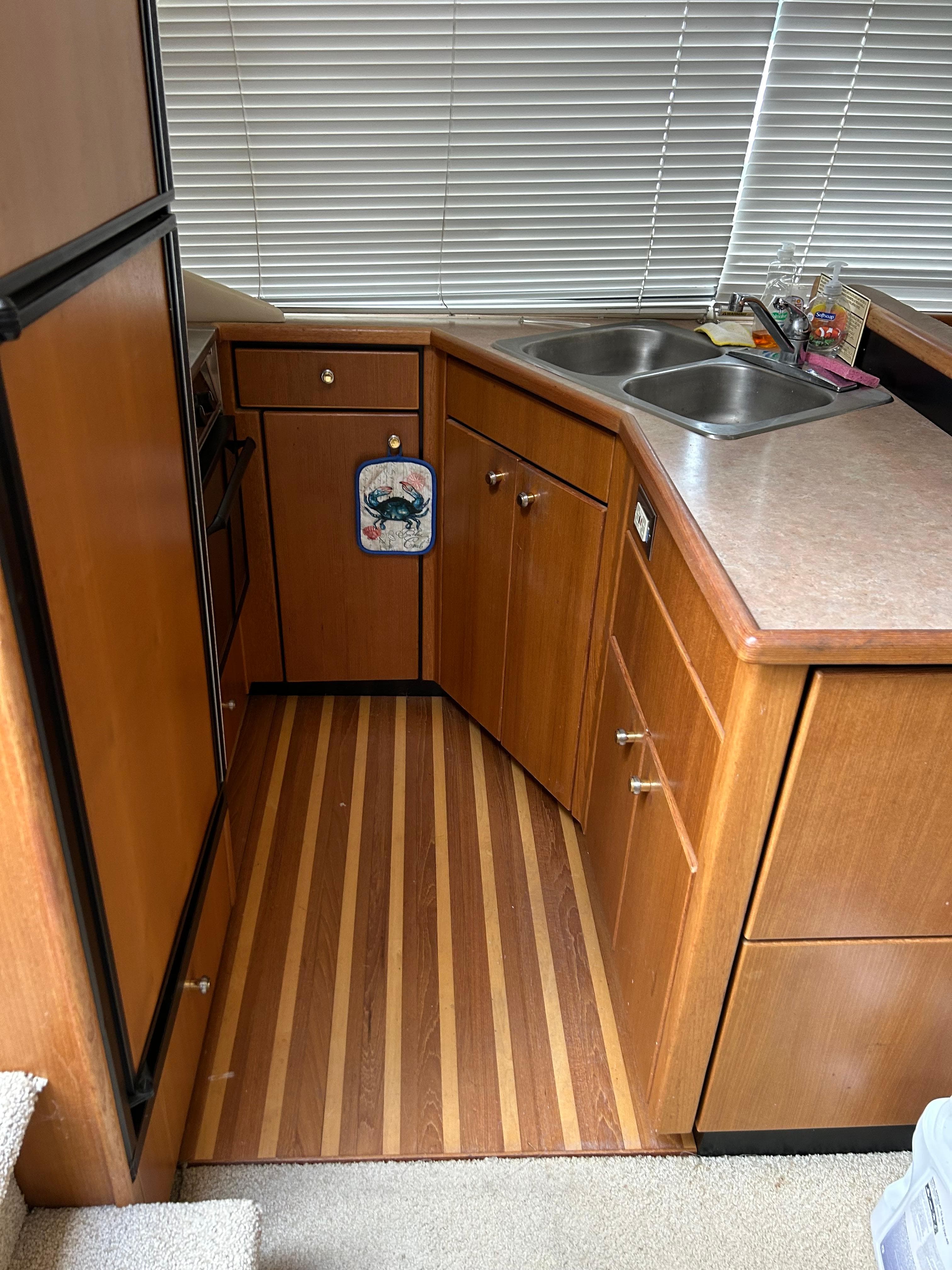 2000 Bayliner 4087 Motoryacht kitchen with wood cabinets, dual sink, and striped flooring.