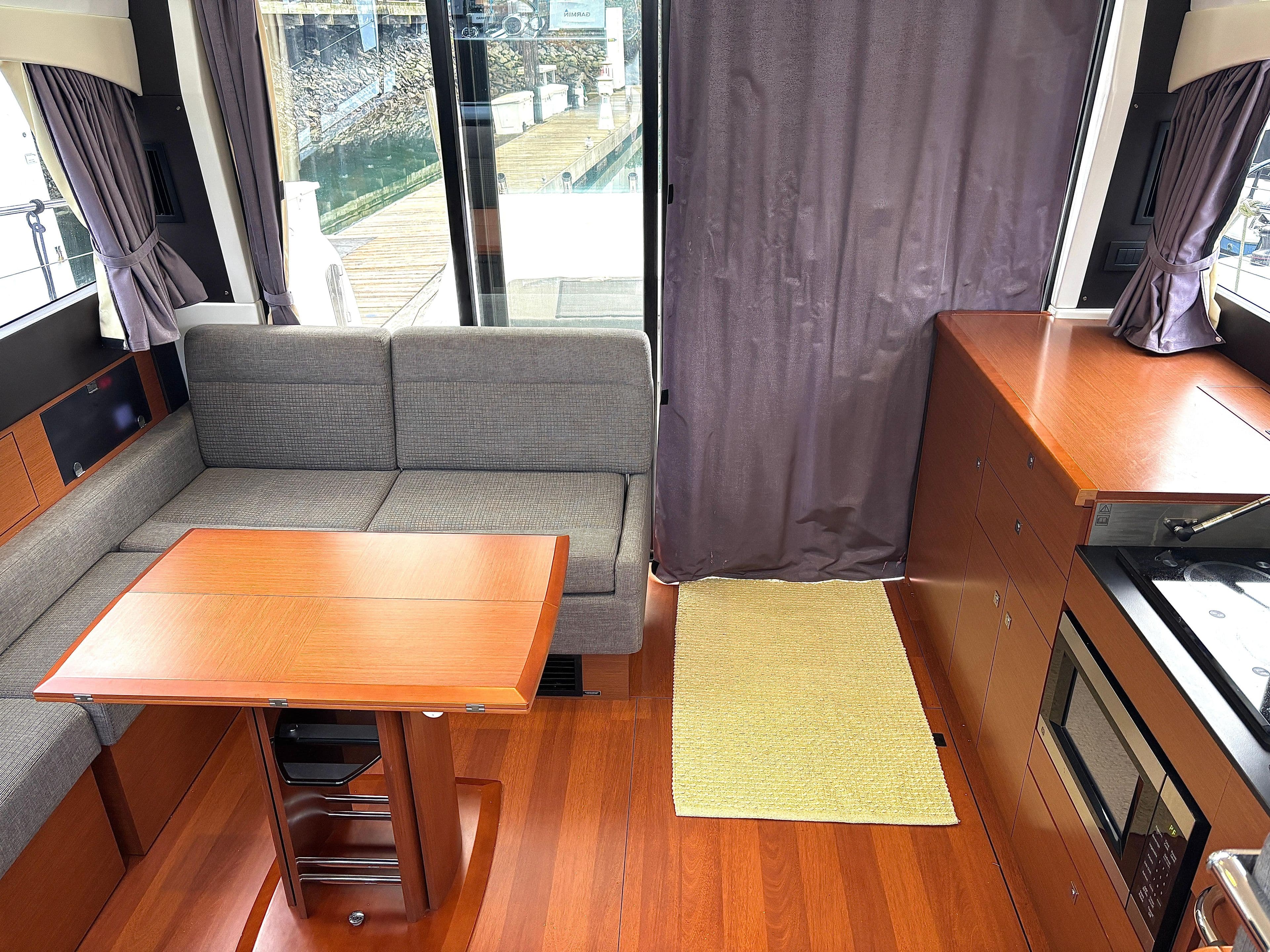 Interior of 2014 Jeanneau NC 14 yacht with wood flooring and cozy seating area.