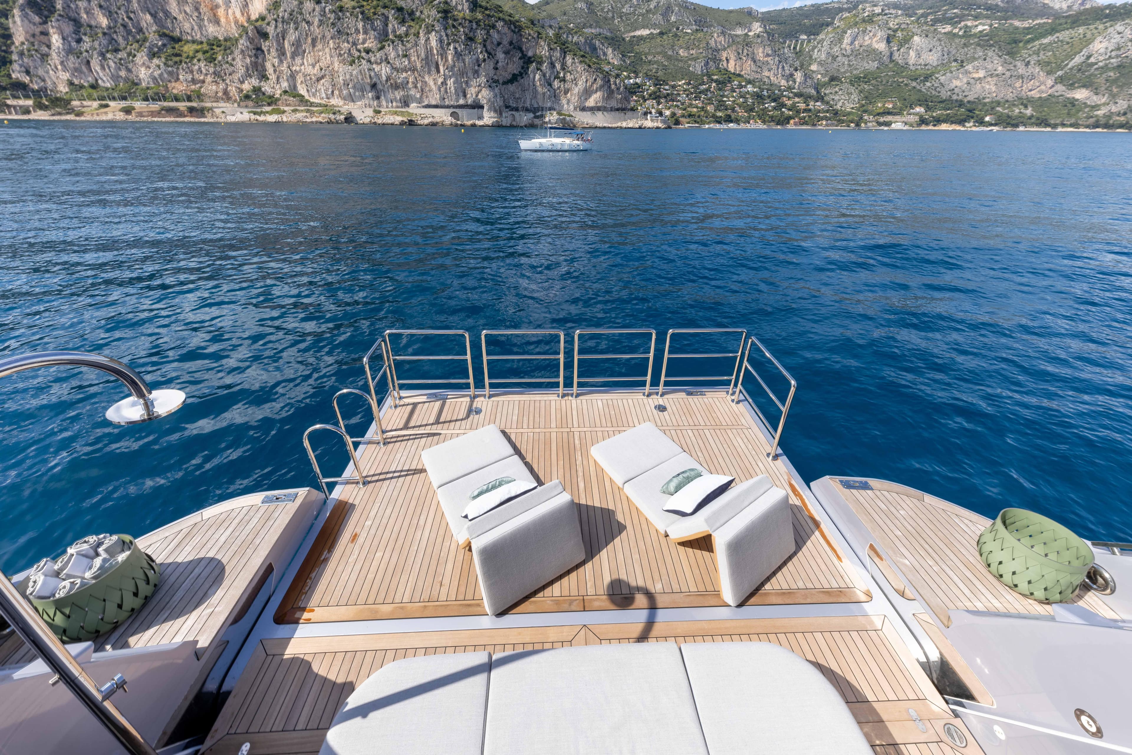 Luxurious Azimut Grande 36M yacht deck with sun loungers, overlooking serene blue waters and rocky coastline.