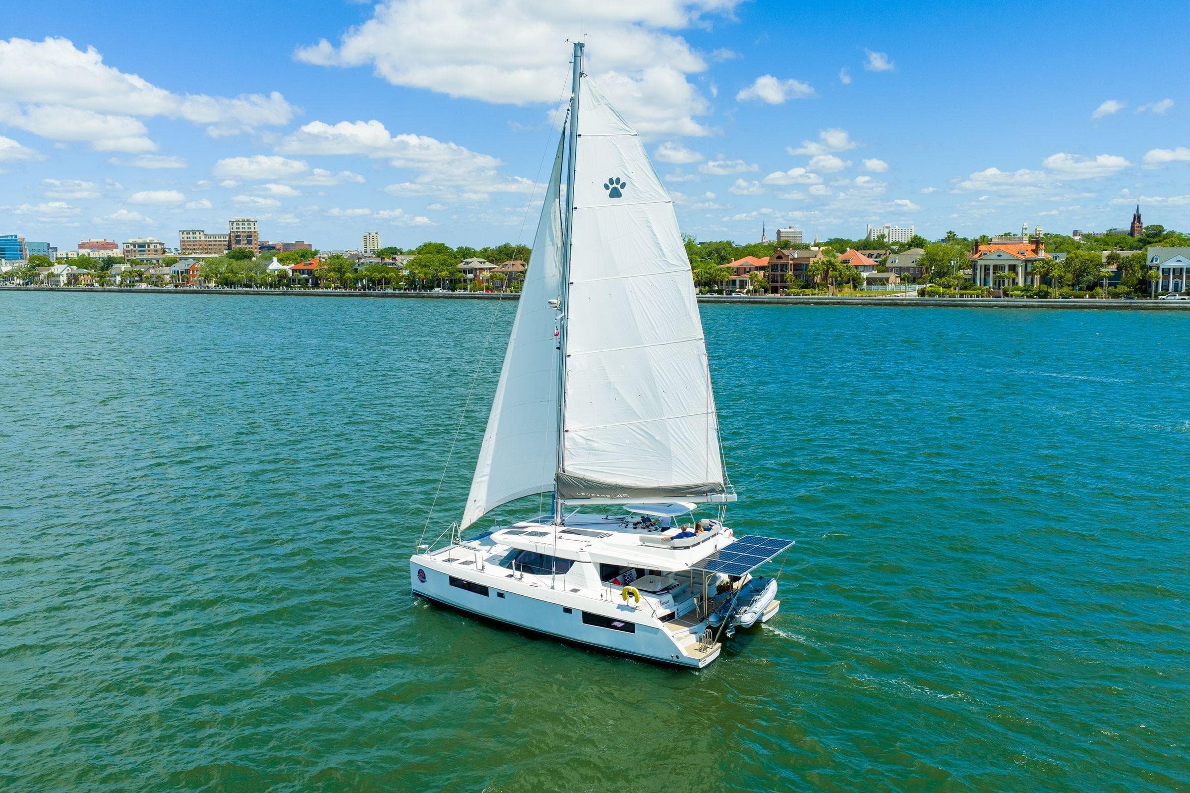 Sailing catamaran Leopard 45, 2020 model, cruising near a scenic coastal cityscape.