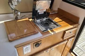 2023 Cutwater C-248 Coupe kitchenette with stove, sink, and wooden cabinetry.
