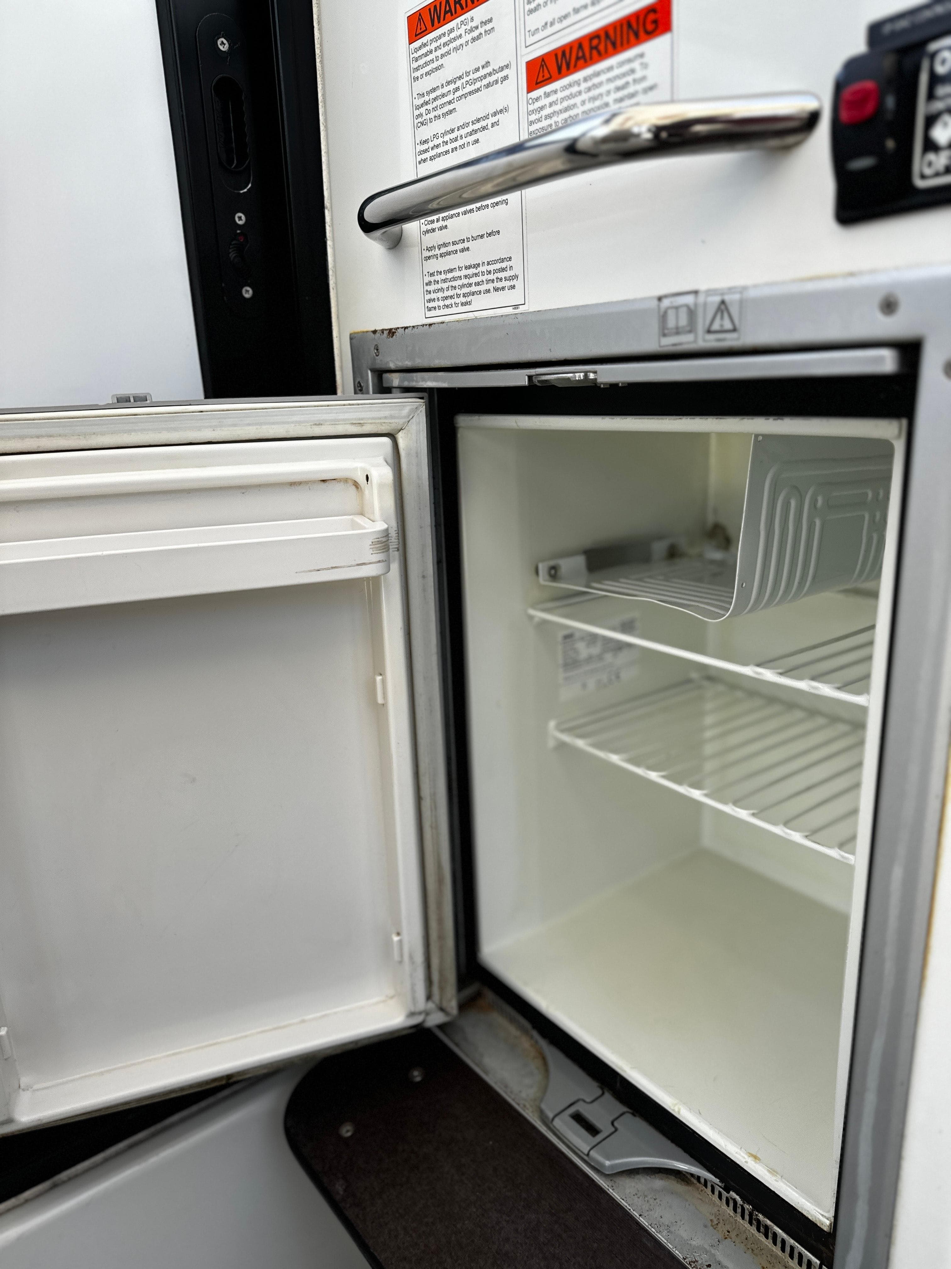 Open refrigerator inside 2016 Jeanneau Merry Fisher 855 Marlin boat, showing shelves and warning labels.