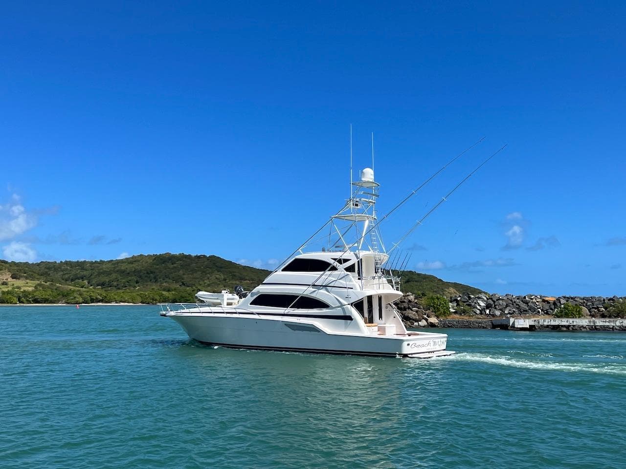 2004 Bertram 670 yacht cruising in clear blue waters near a green island.