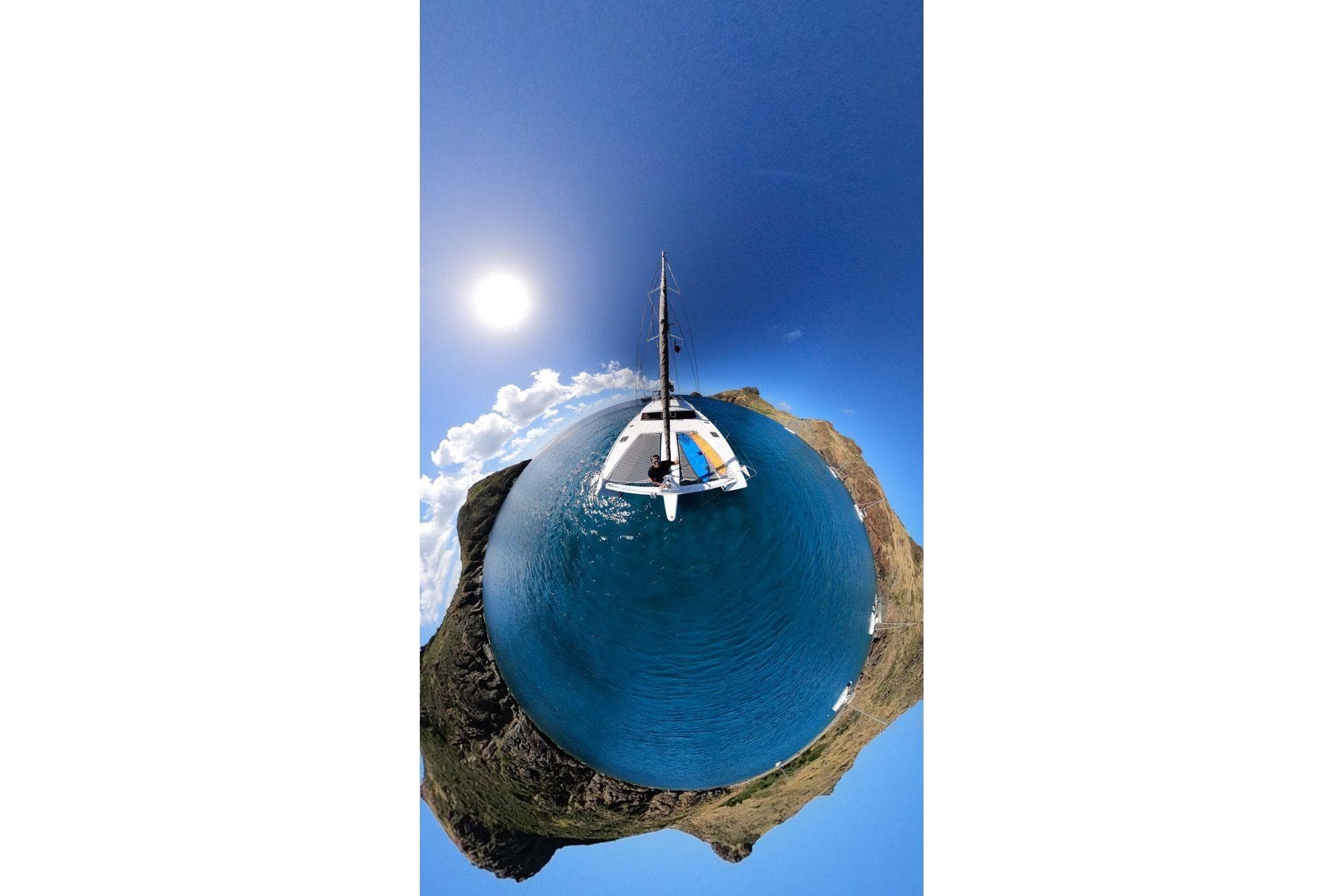Aerial view of 2014 FONTAINE PAJOT 63 yacht on blue ocean, surrounded by rocky landscape.