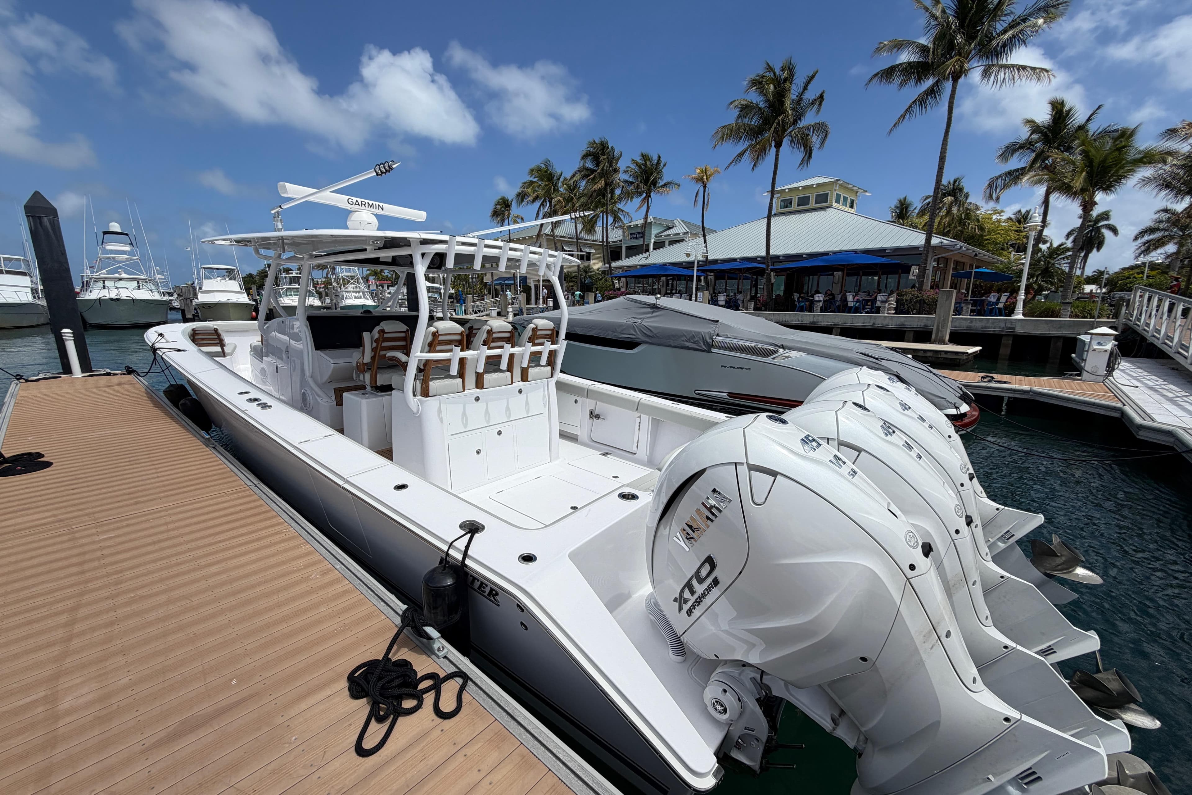 2026 Jupiter 43 boat docked at marina with triple outboard engines, palm trees, and blue sky.