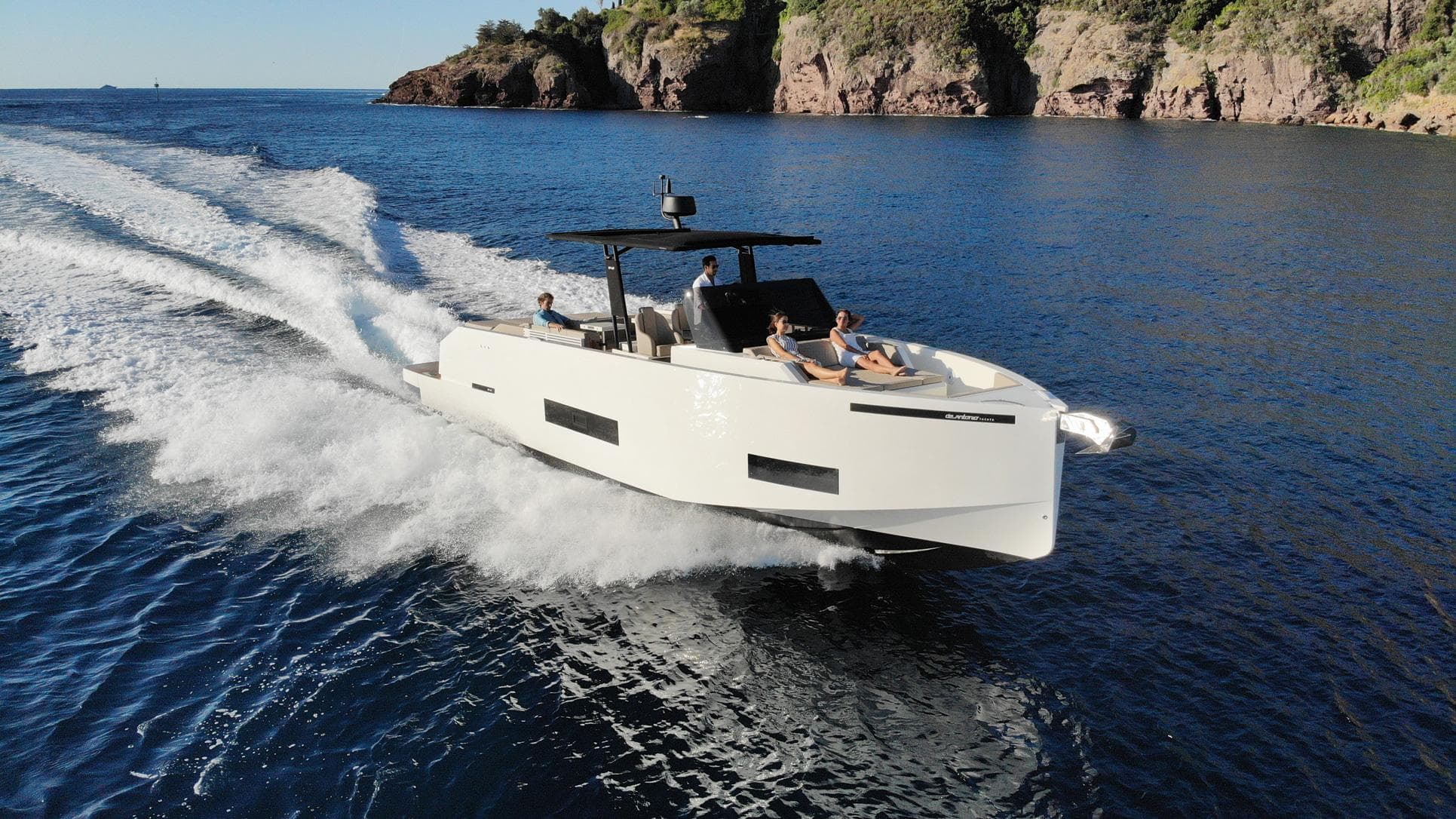 2024 De Antonio Yachts D42 Open cruising on blue ocean near rocky coastline.