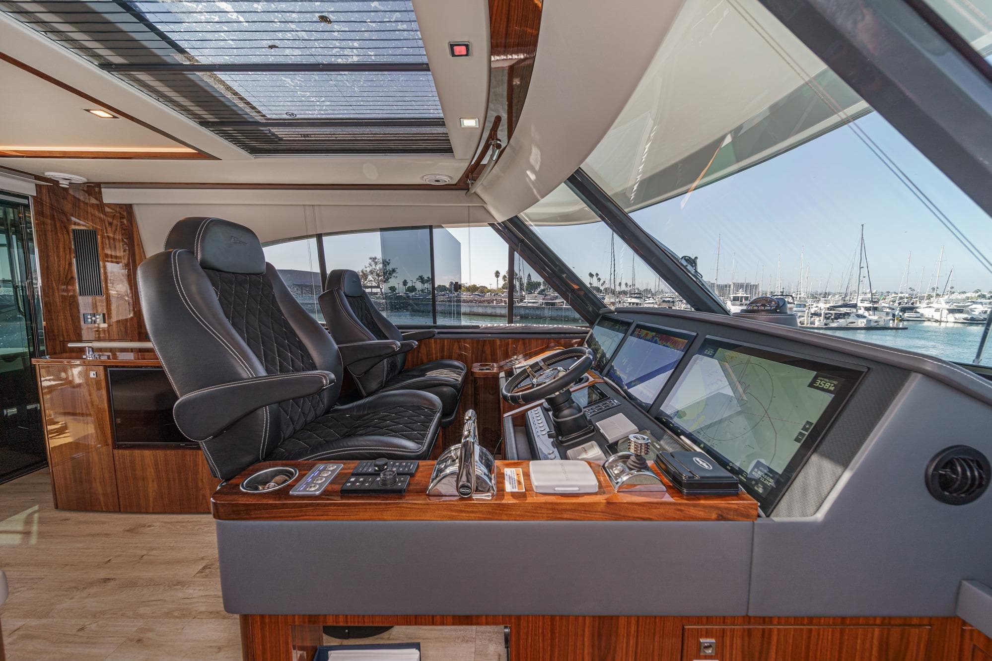 Luxurious helm of 2023 Riviera 64 Sports Motor Yacht with panoramic marina view.