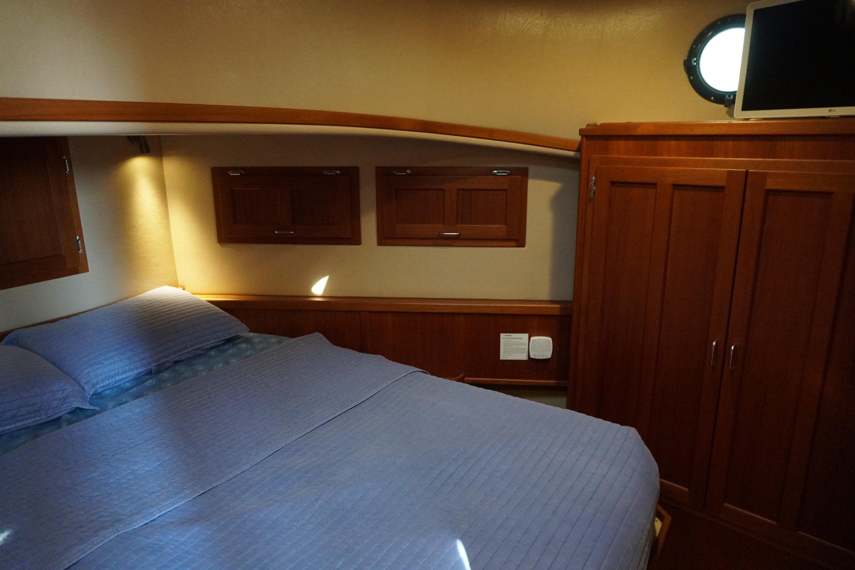 Cozy cabin interior of 2004 American Tug 34 with bed, wooden cabinets, and porthole window.