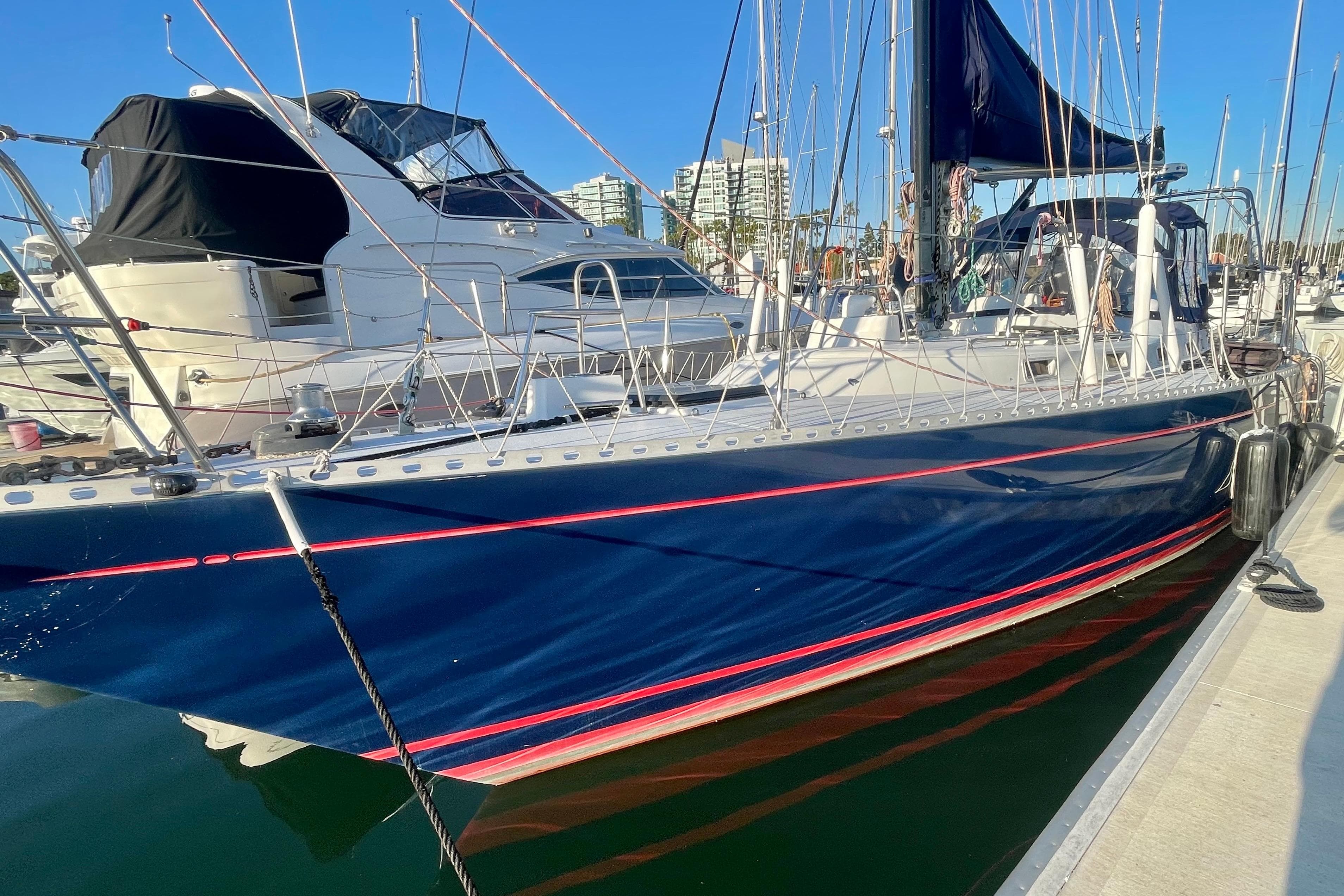 1982 Stevens cutter sailboat docked in marina, blue hull with red stripe, clear sky.