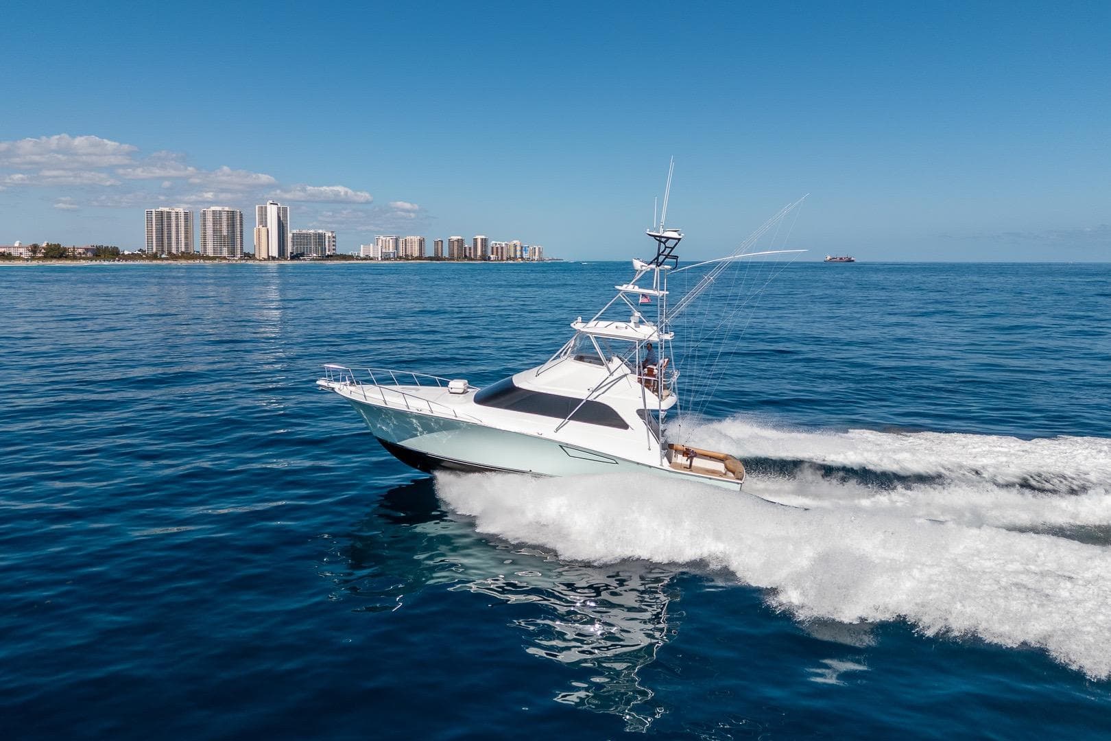 2009 Cabo 52 Flybridge yacht cruising on blue ocean near city skyline.