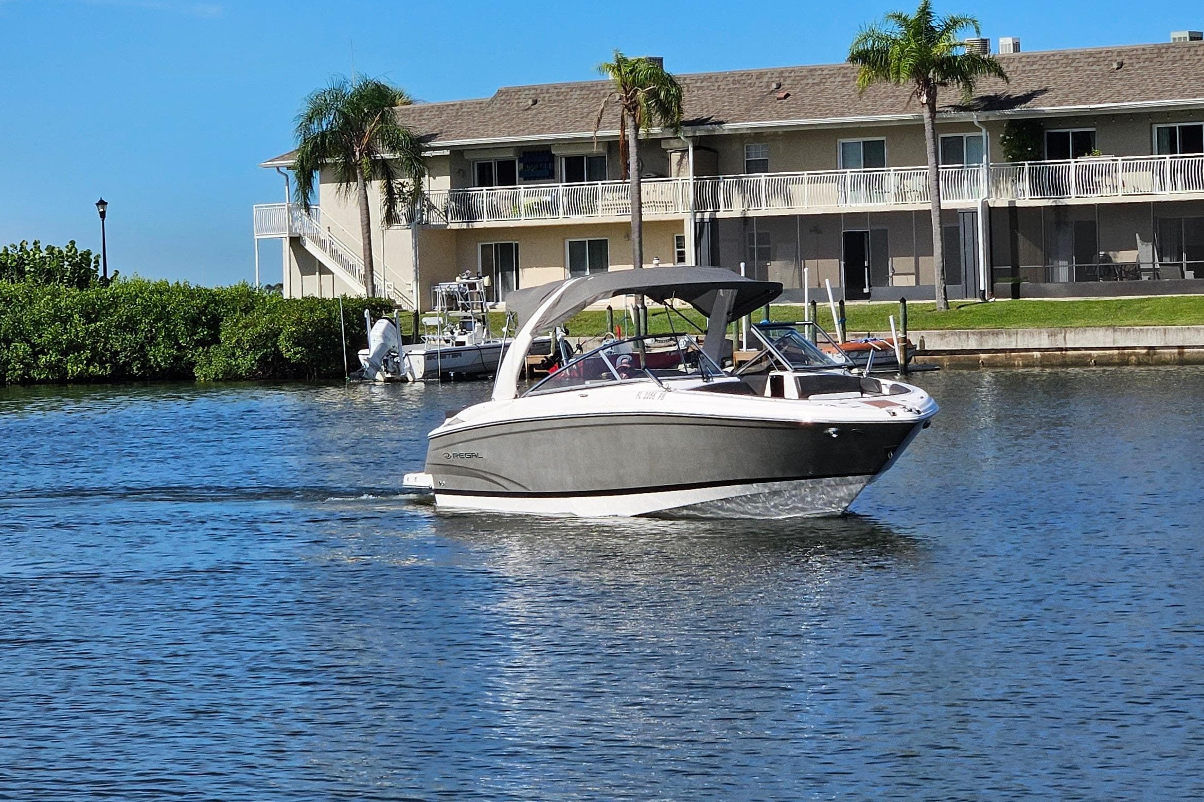 2010 Regal 2700 ES Bowrider cruising on a sunny waterfront near residential buildings.