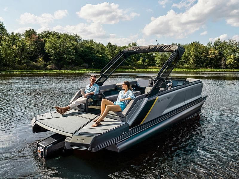 2024 Manitou EXPLORE 24 SWITCHBACK pontoon boat on a serene lake with two people relaxing.