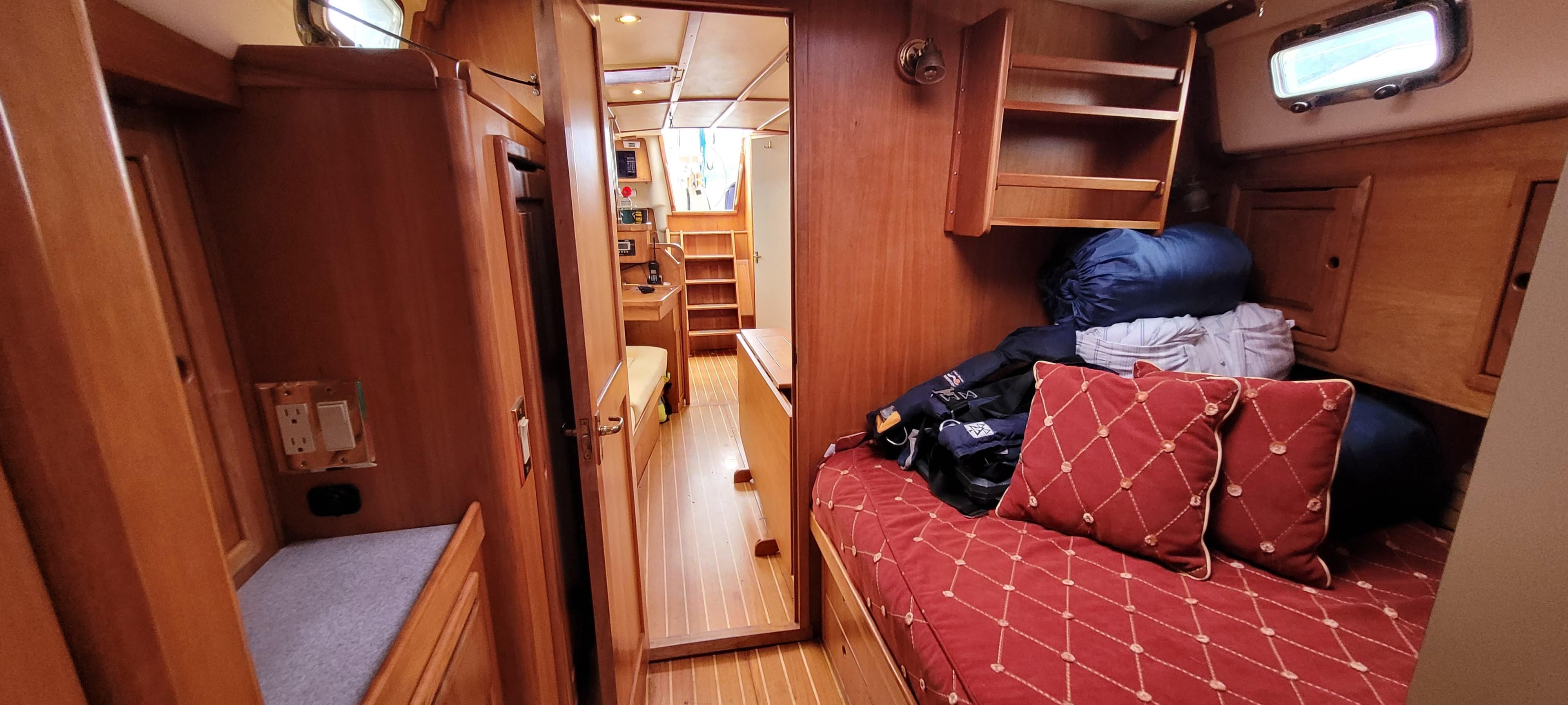 Cozy interior of 1997 Saga 43 sailboat with wooden furnishings and red-patterned bedding.