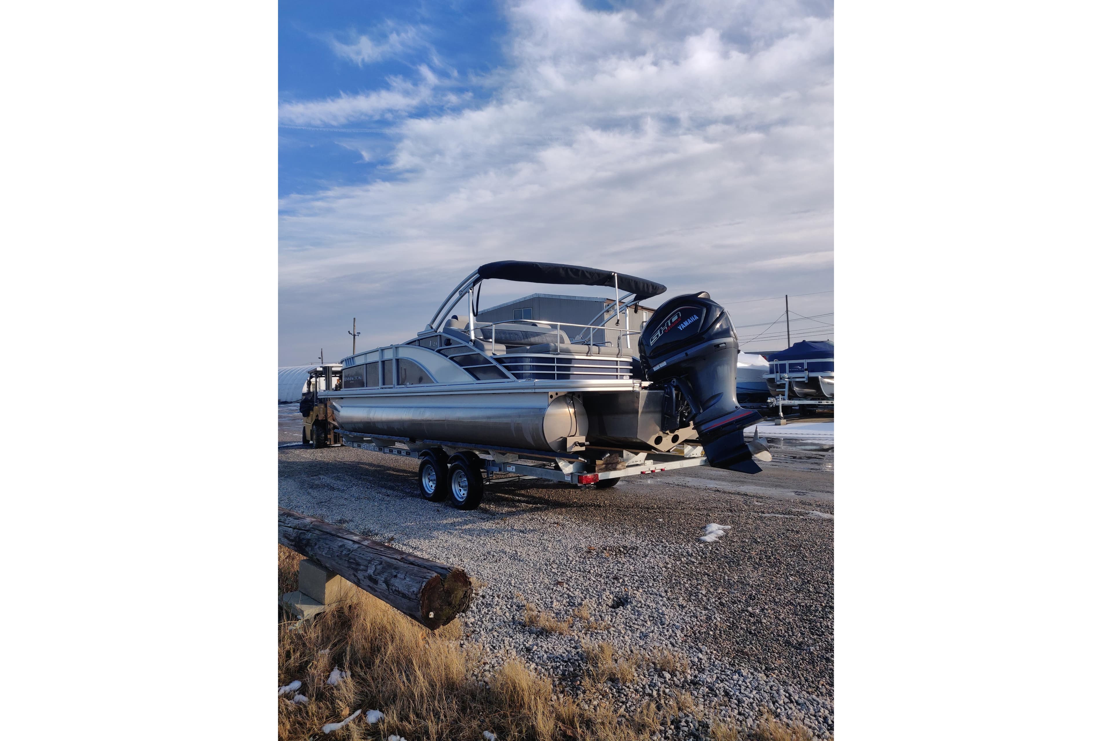 2023 Bennington 23LTSB pontoon boat on trailer, parked on gravel with cloudy sky.