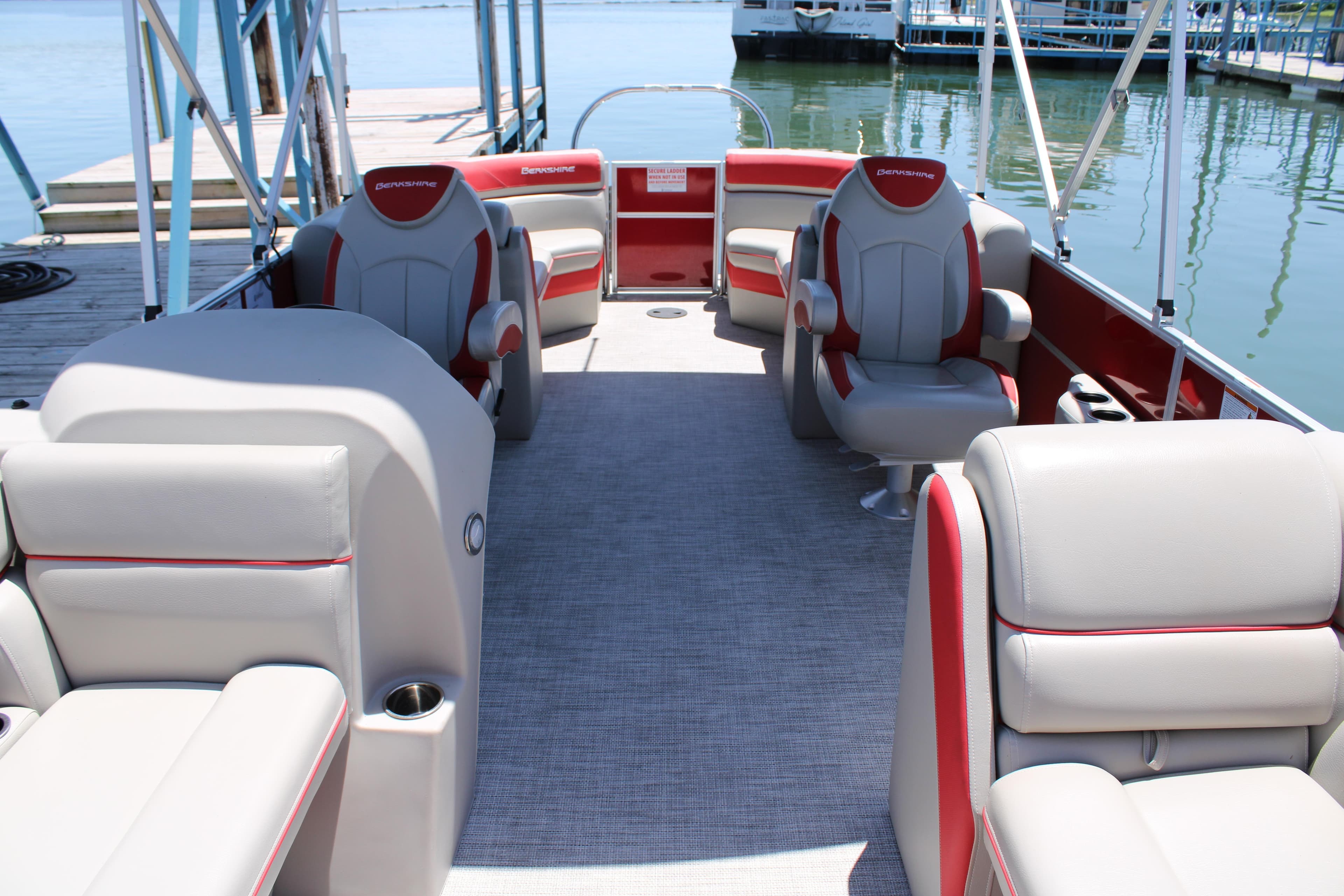 2024 Berkshire 24RFX LE pontoon boat interior with gray and red seating, docked by the water.