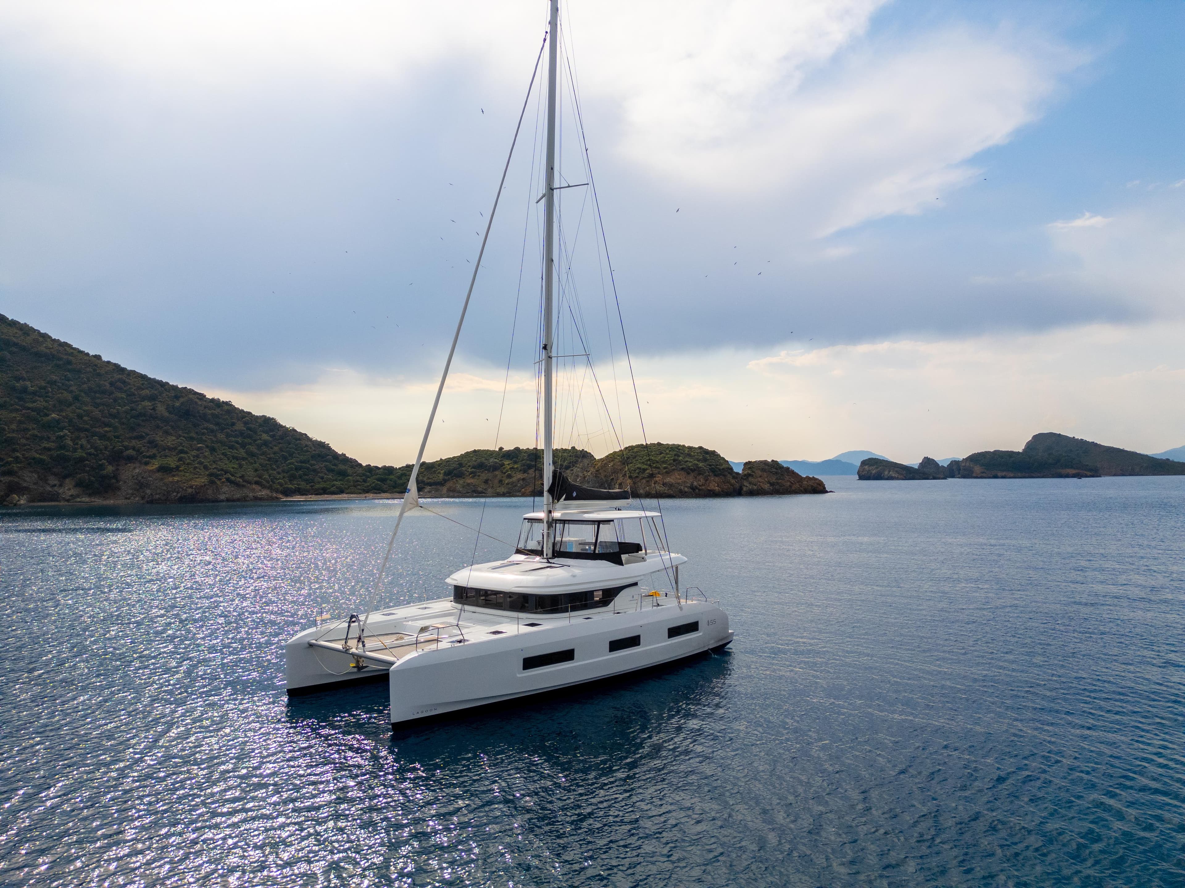 2024 Lagoon 55 catamaran sailing in serene waters with scenic island backdrop.