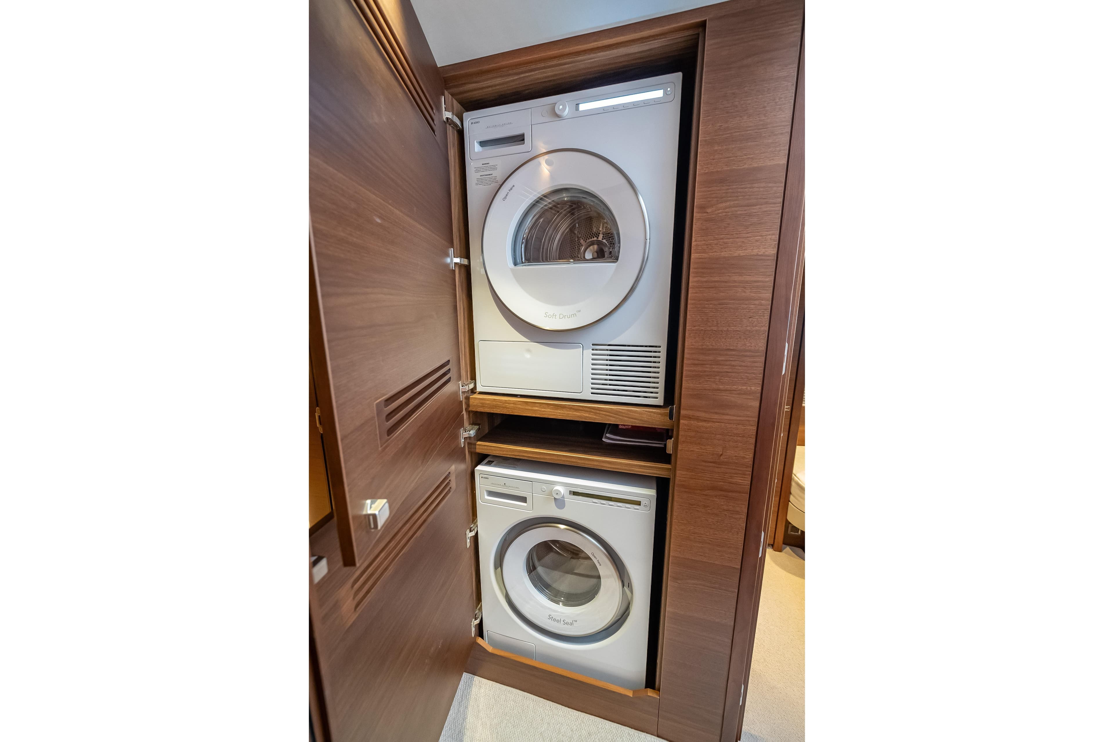 Stacked washer and dryer in 2023 Princess Y72 yacht's wooden cabinet.