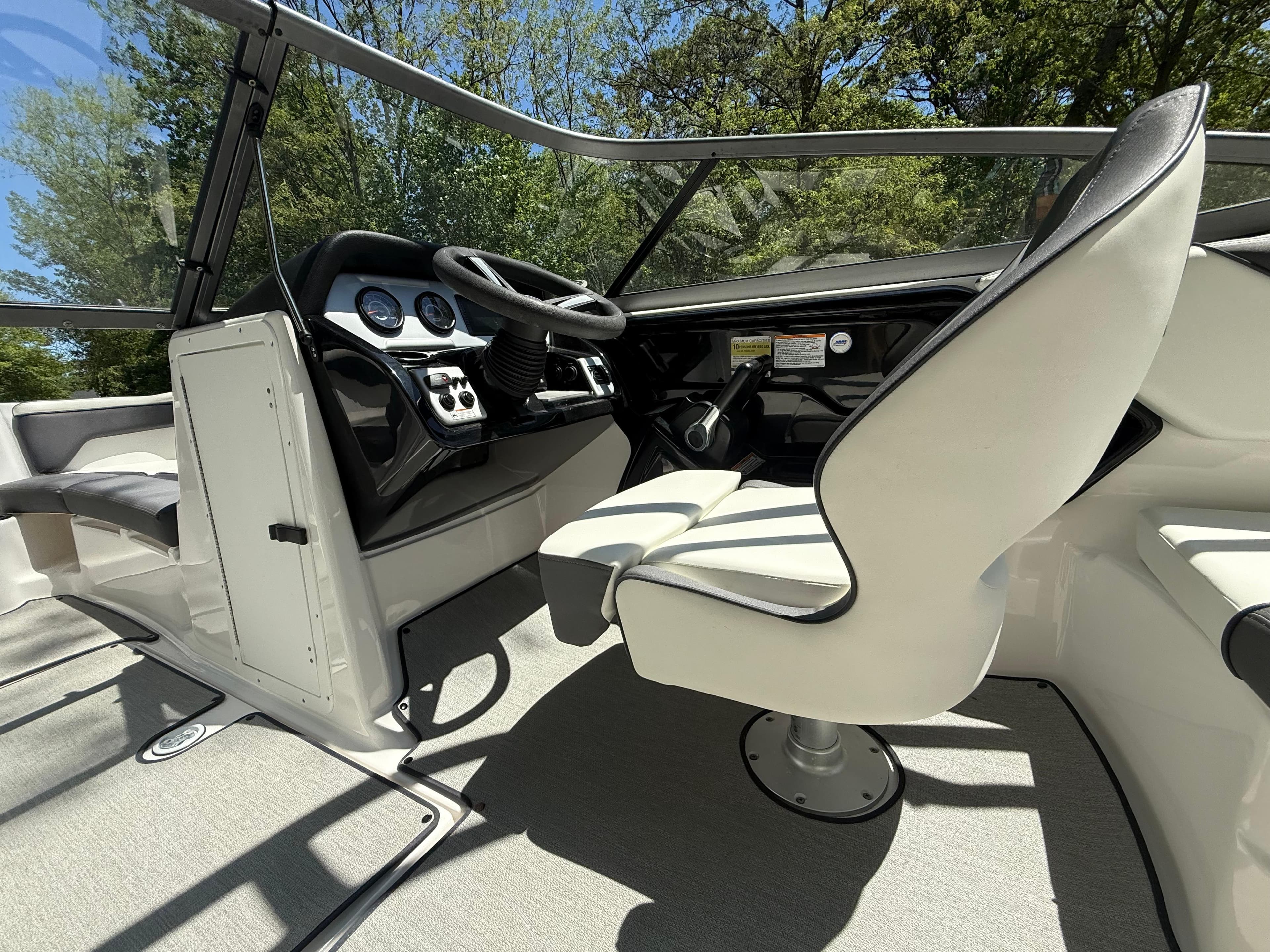 2022 Yamaha Boats AR210 cockpit with steering wheel and seating, surrounded by trees.